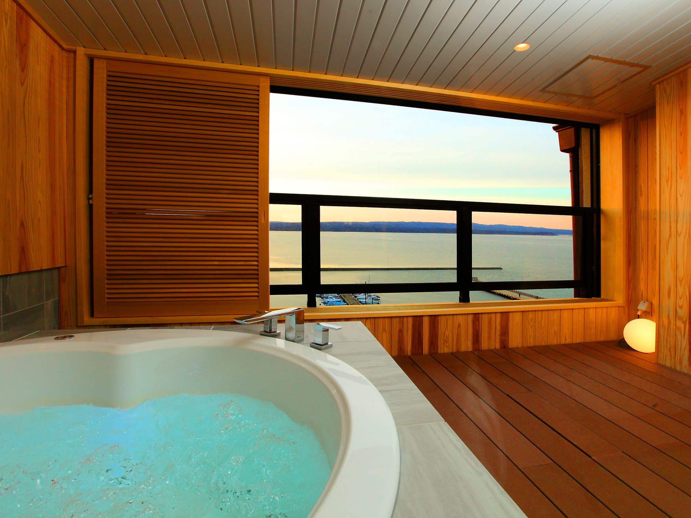 Guest room with private round jacuzzi tub and cedar deck overlooking Nanao Bay at dusk, Noshu Iroha