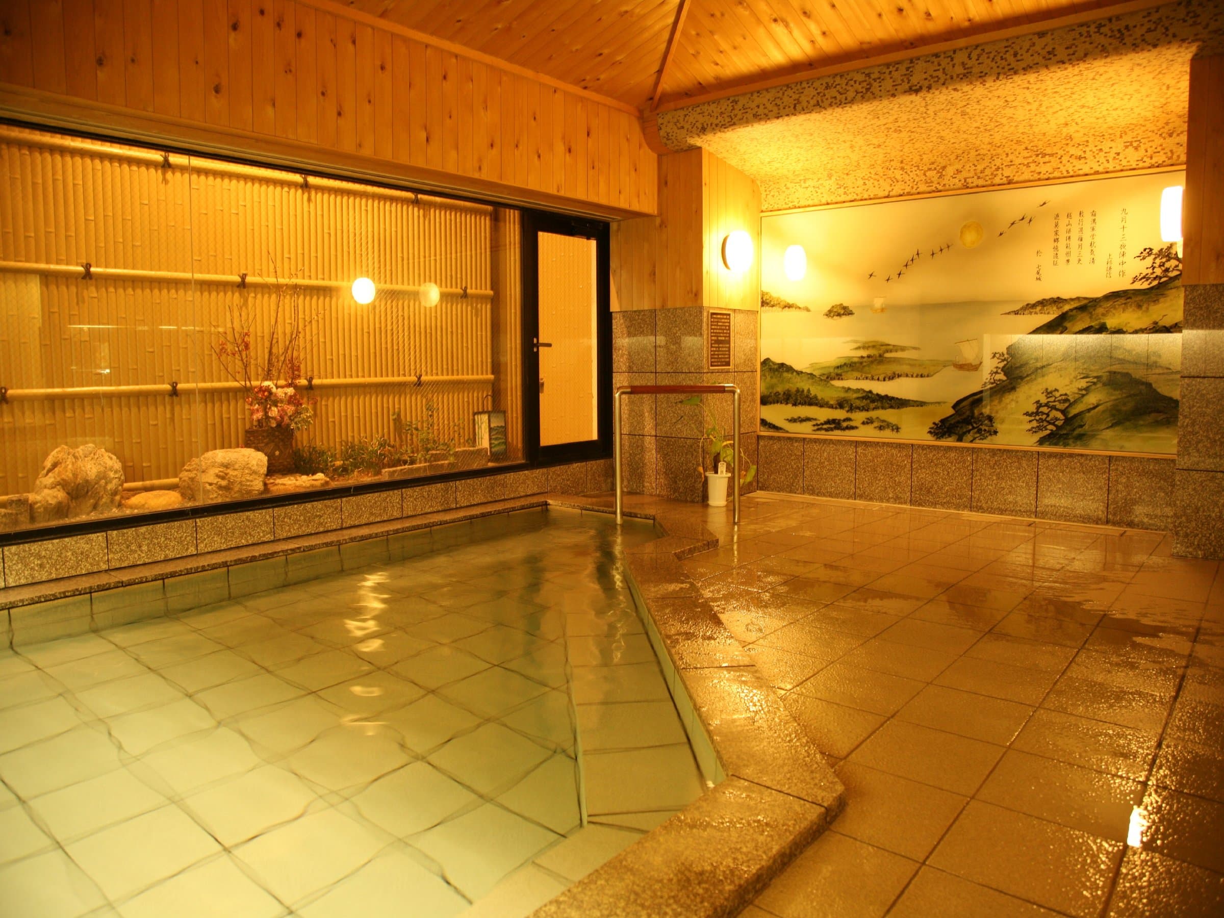 Indoor public onsen bath at Noshu Iroha with painted seascape mural and bamboo garden through the window