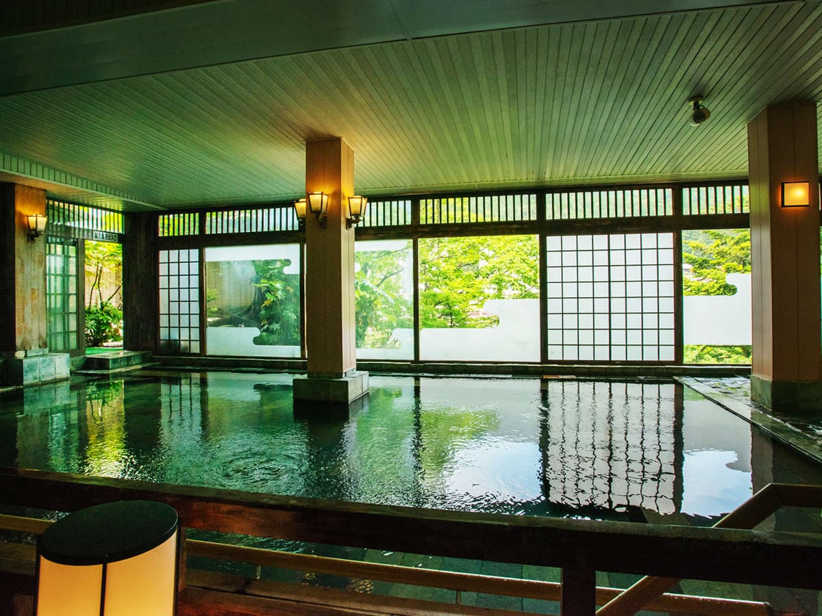 Indoor hot-spring bath with shoji windows and tatami-edged pool framing the green garden at Kinugawa Park Hotels