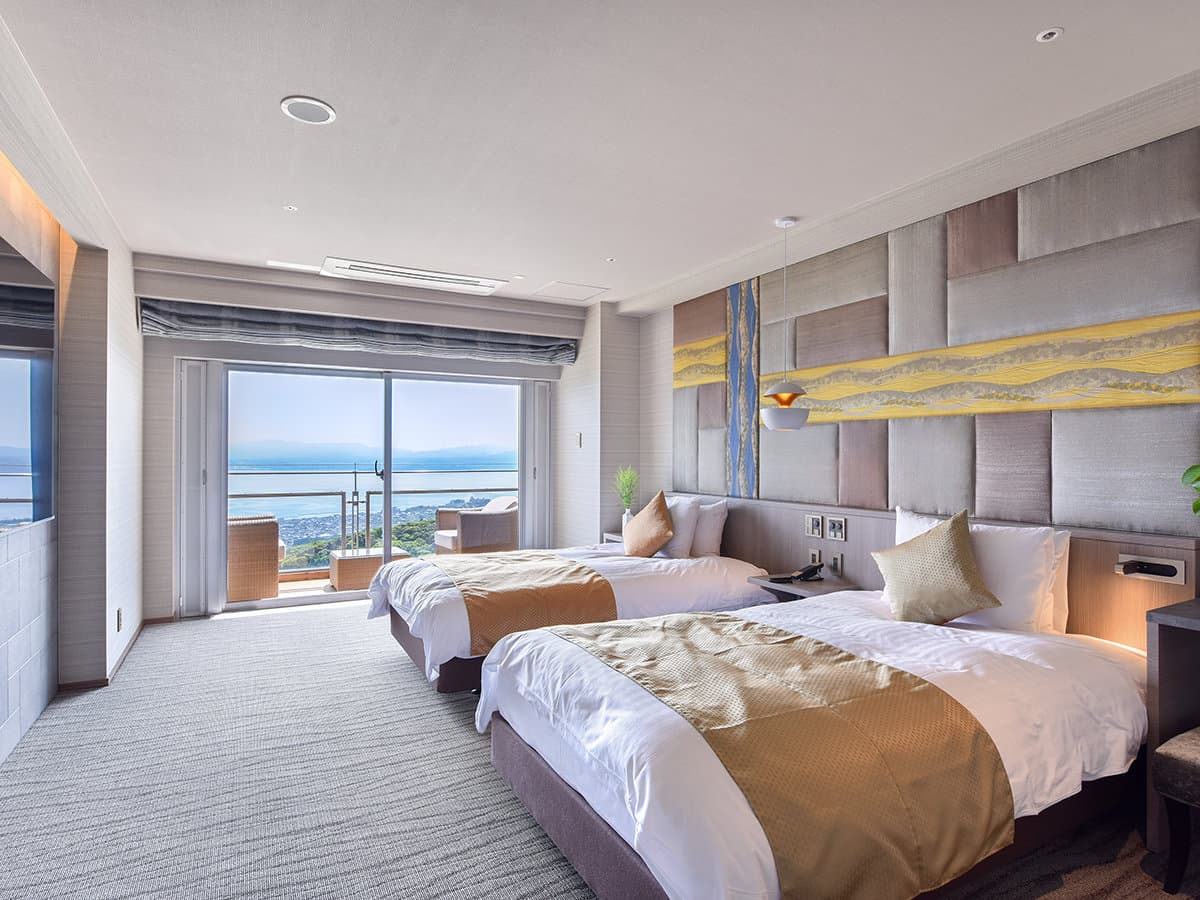 Bright twin guest room at Bettei Amafuru Oka with floor-to-ceiling windows framing the Ibusuki sea view