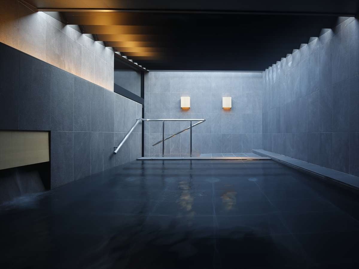 Indoor onsen bath at SOKI ATAMI lined in dark grey stone with soft wall lighting