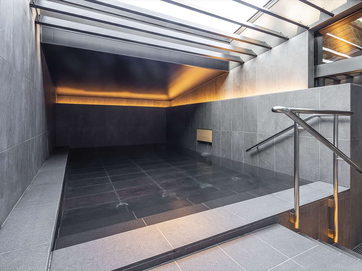Semi-open hot spring bath at SOKI ATAMI with steaming water under a slatted roof