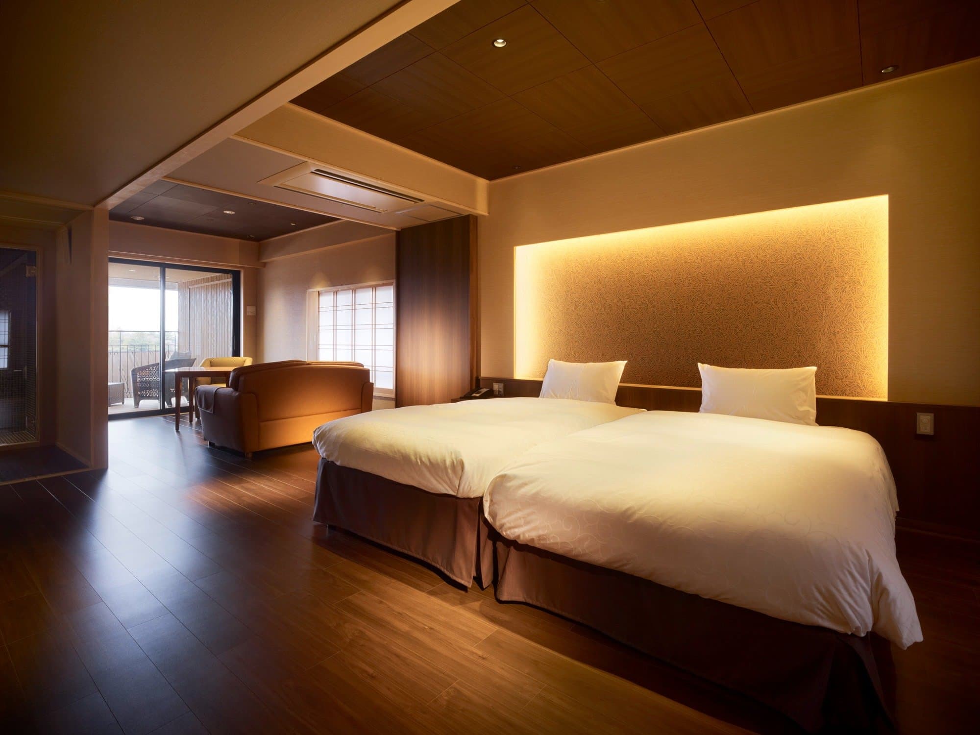 Spacious twin-bed guest room with warm wood floors, sofa and a private balcony at Sanshi Suimei in Shuzenji Onsen