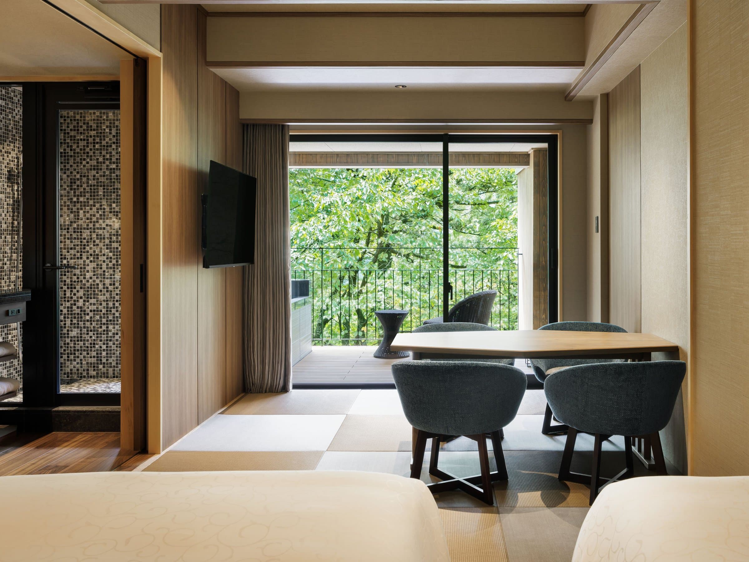 Modern Japanese guest room with tatami, dining table and a sliding-door terrace framing green forest at Sanshi Suimei, Izu