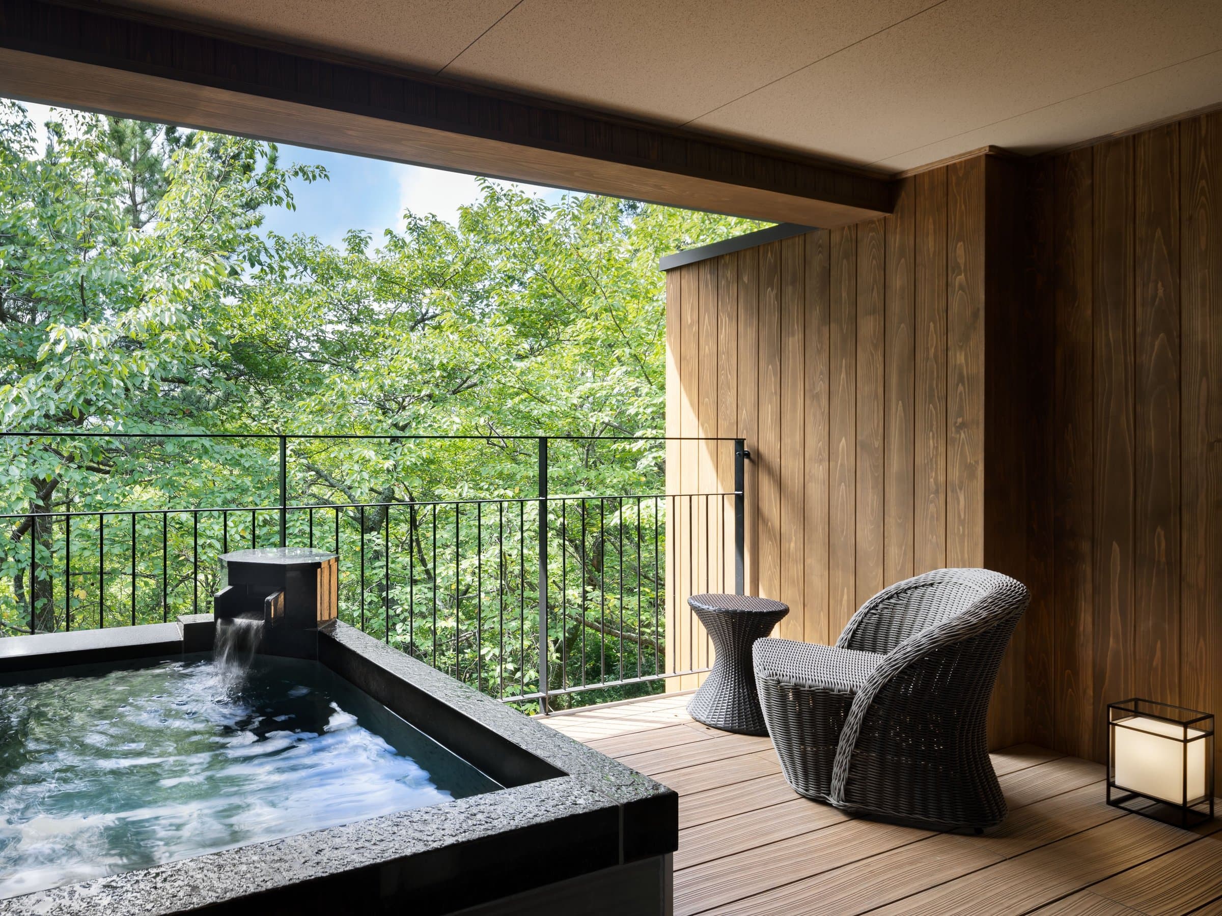 Private open-air stone bath on a wooden terrace with a rattan chair overlooking forest at Sanshi Suimei, Izu