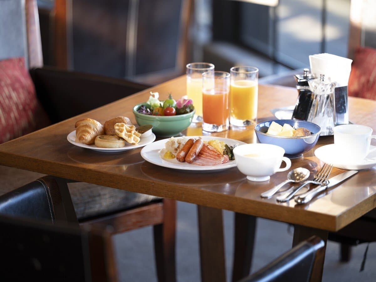 Morning breakfast set with sausages, salad, pastries and fresh juice on a wooden table at Sanshi Suimei in Shuzenji Onsen