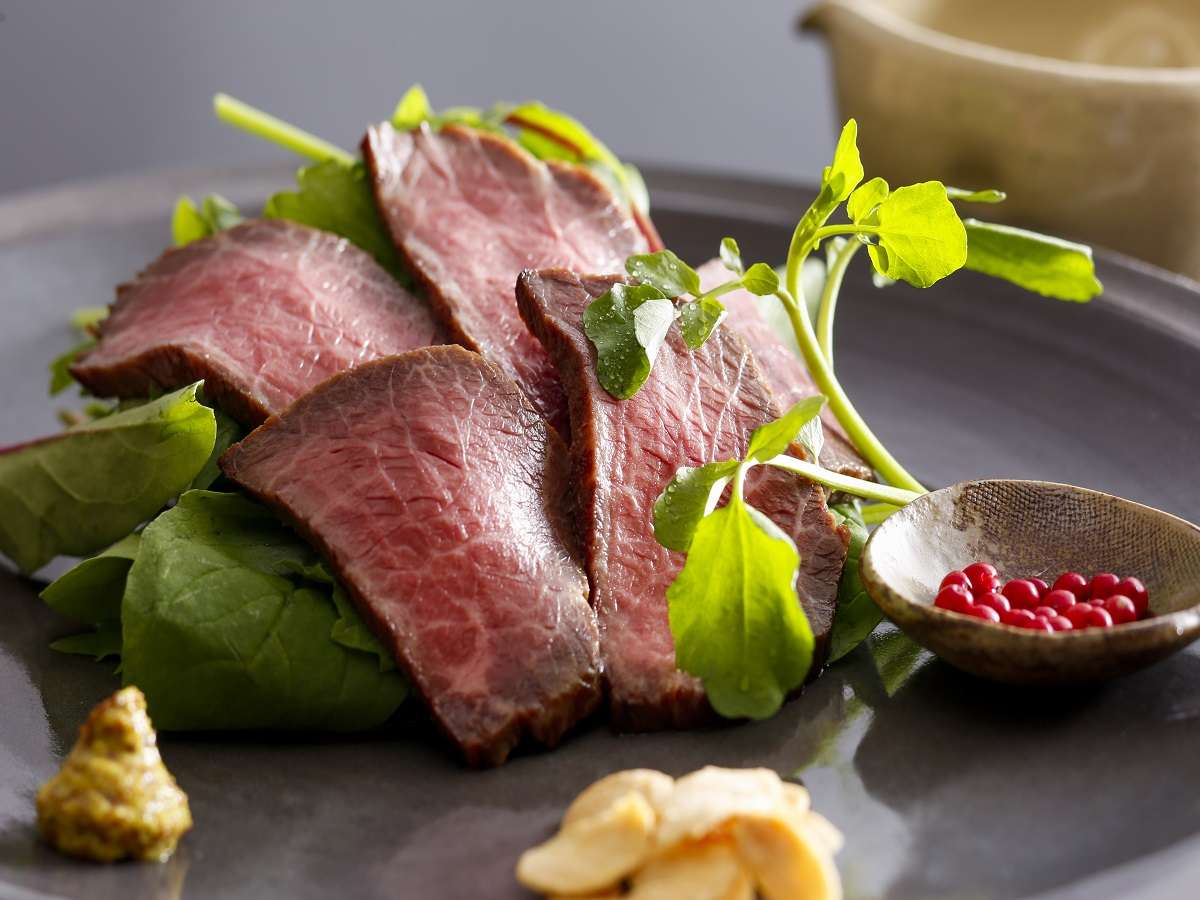 Sliced Kobe beef roast-beef kaiseki course on a dark plate with watercress and pink peppercorns at Spa Terrace Shisui