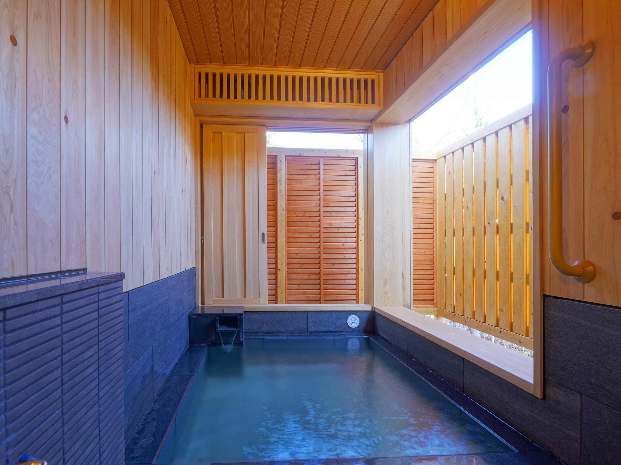 Indoor wooden onsen bath with milky hot-spring water and slatted privacy screen