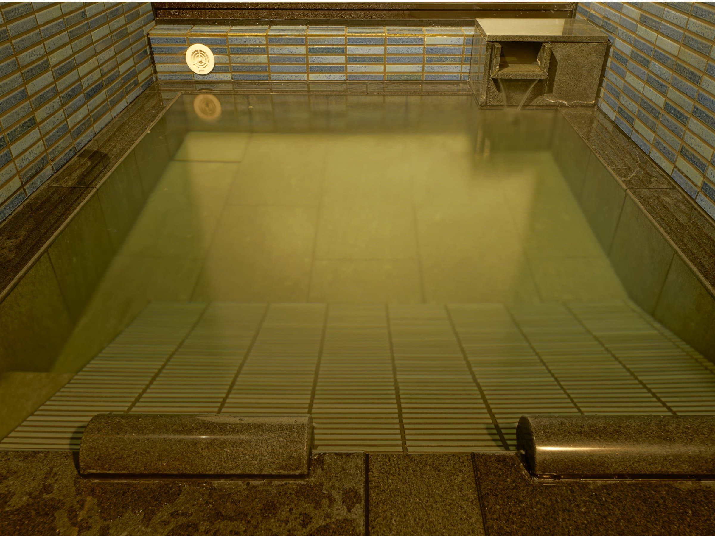 Steamy indoor onsen bath with tiled walls and pale mineral-rich water