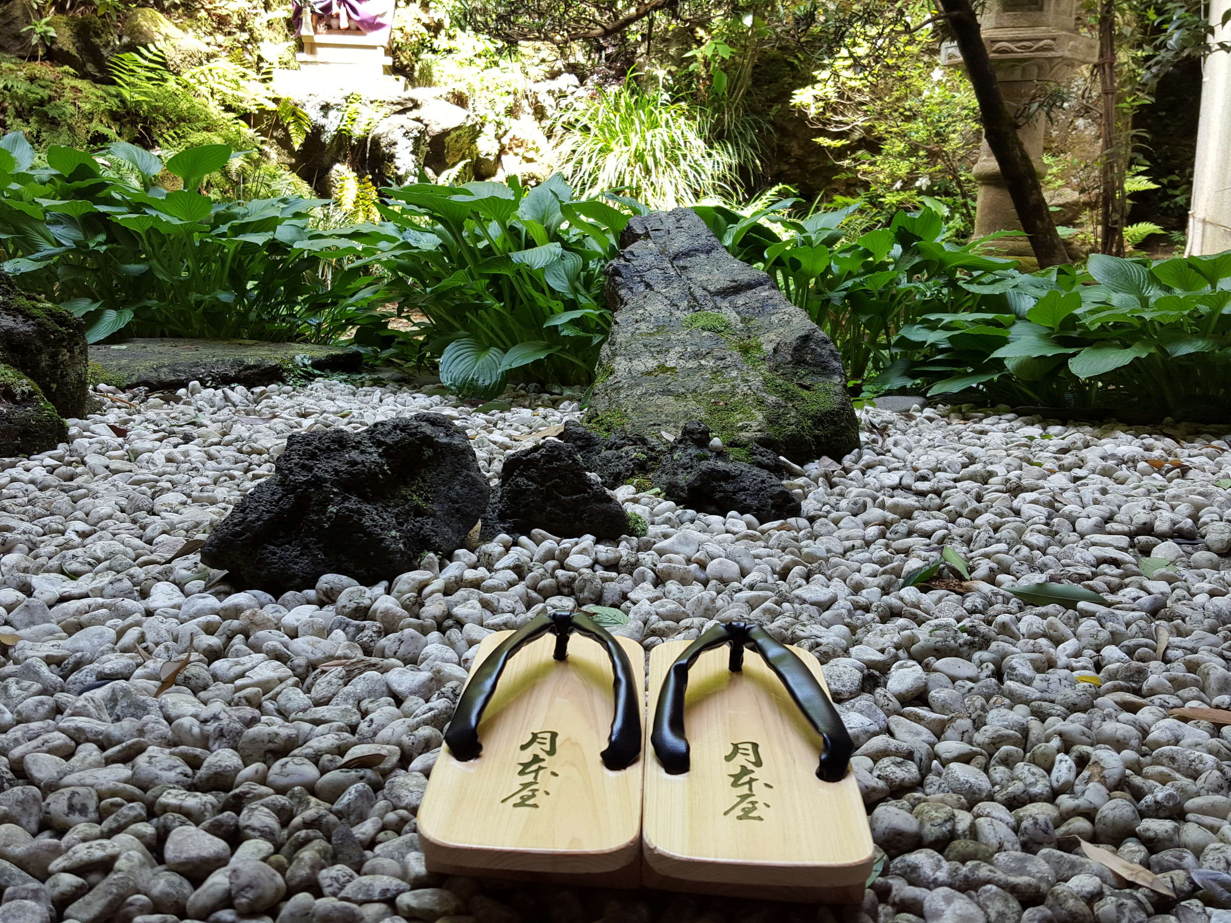 Inner garden of raked gravel and mossy rocks with wooden geta sandals set before greenery, Tsukimotoya, Kinosaki Onsen