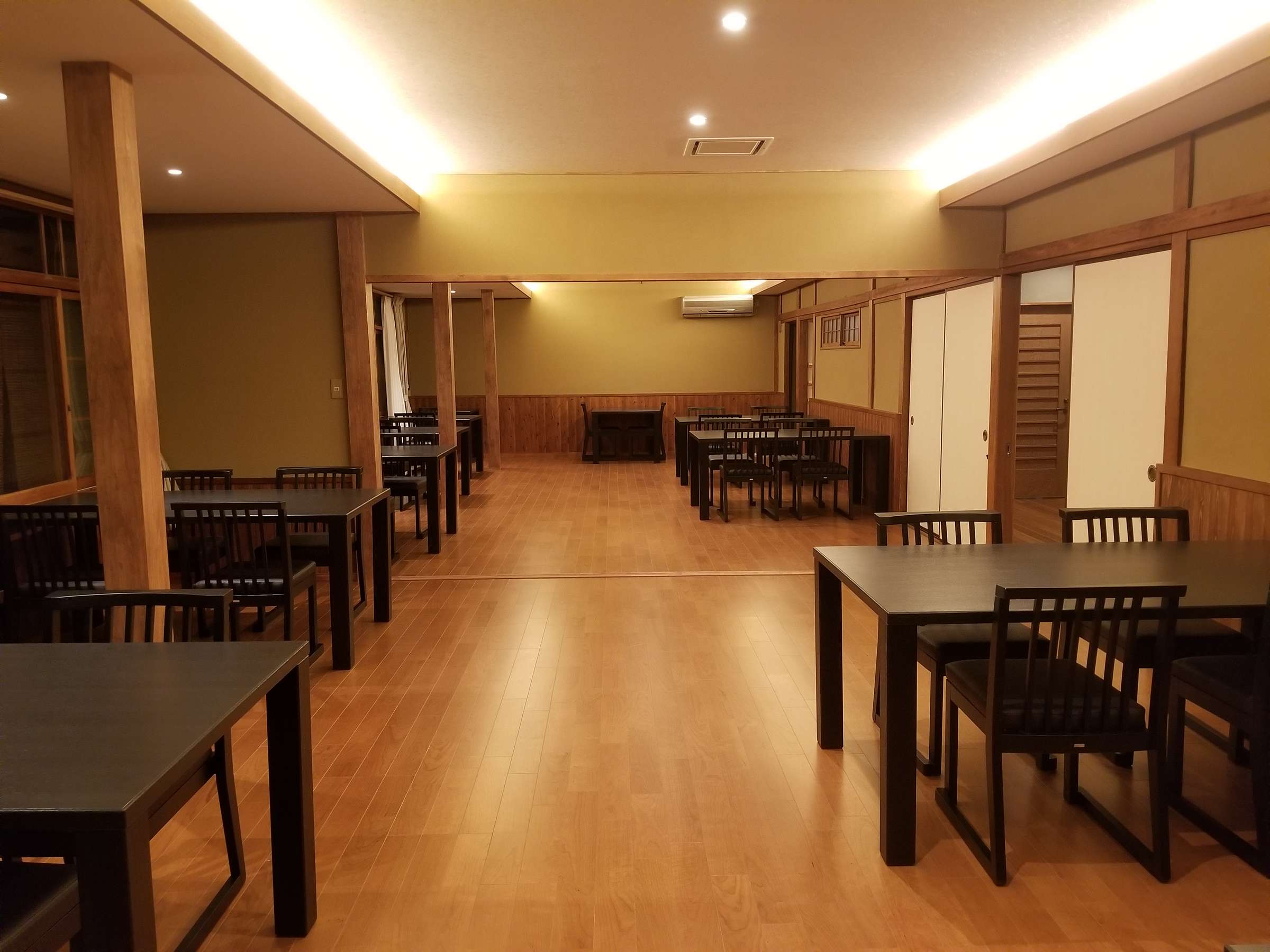Spacious dining hall with dark wood tables and warm cove lighting set for dinner, Tsukimotoya, Kinosaki Onsen