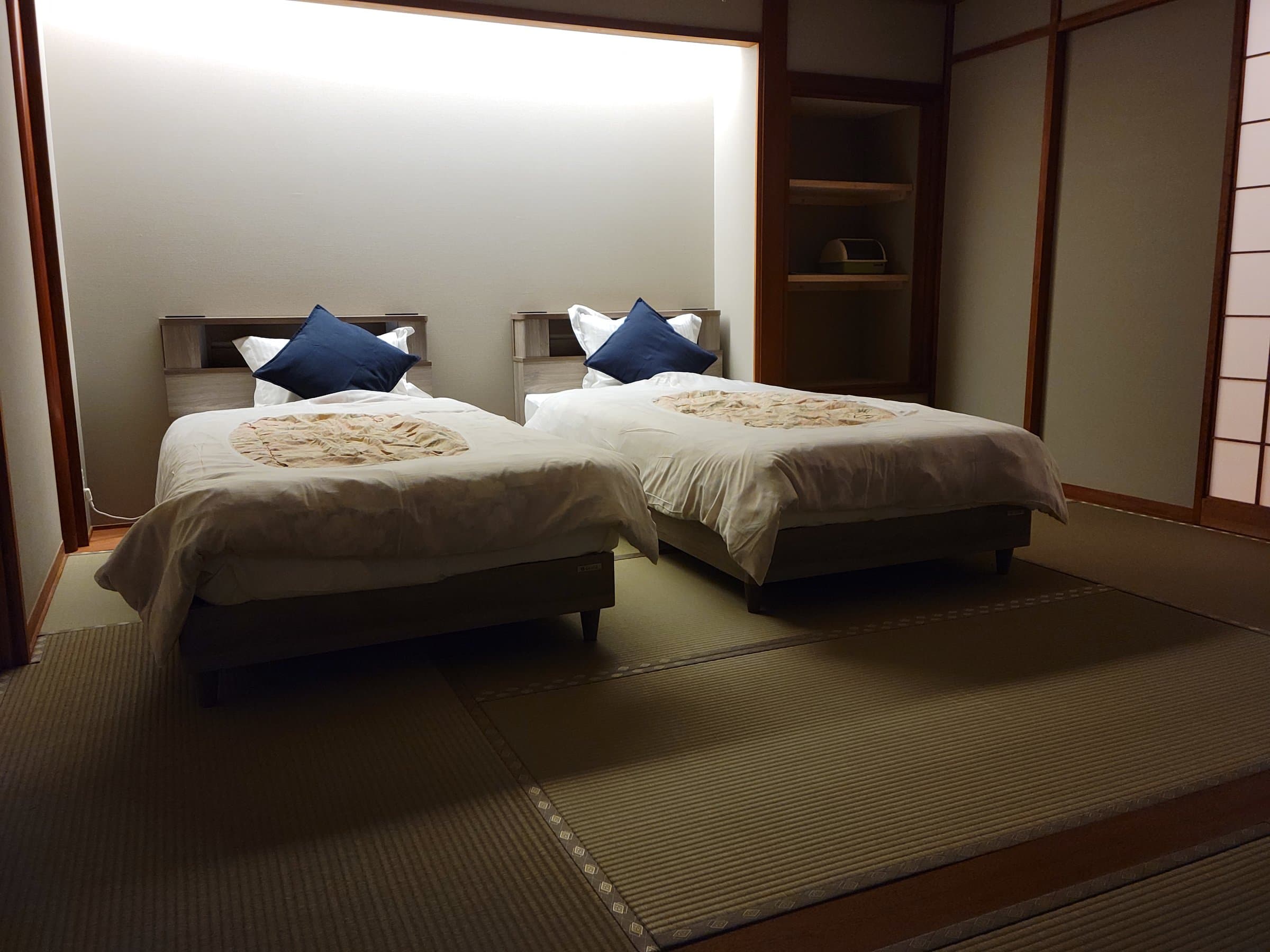 Tatami guest room with two low twin beds and navy pillows beside a recessed shelf, Tsukimotoya, Kinosaki Onsen
