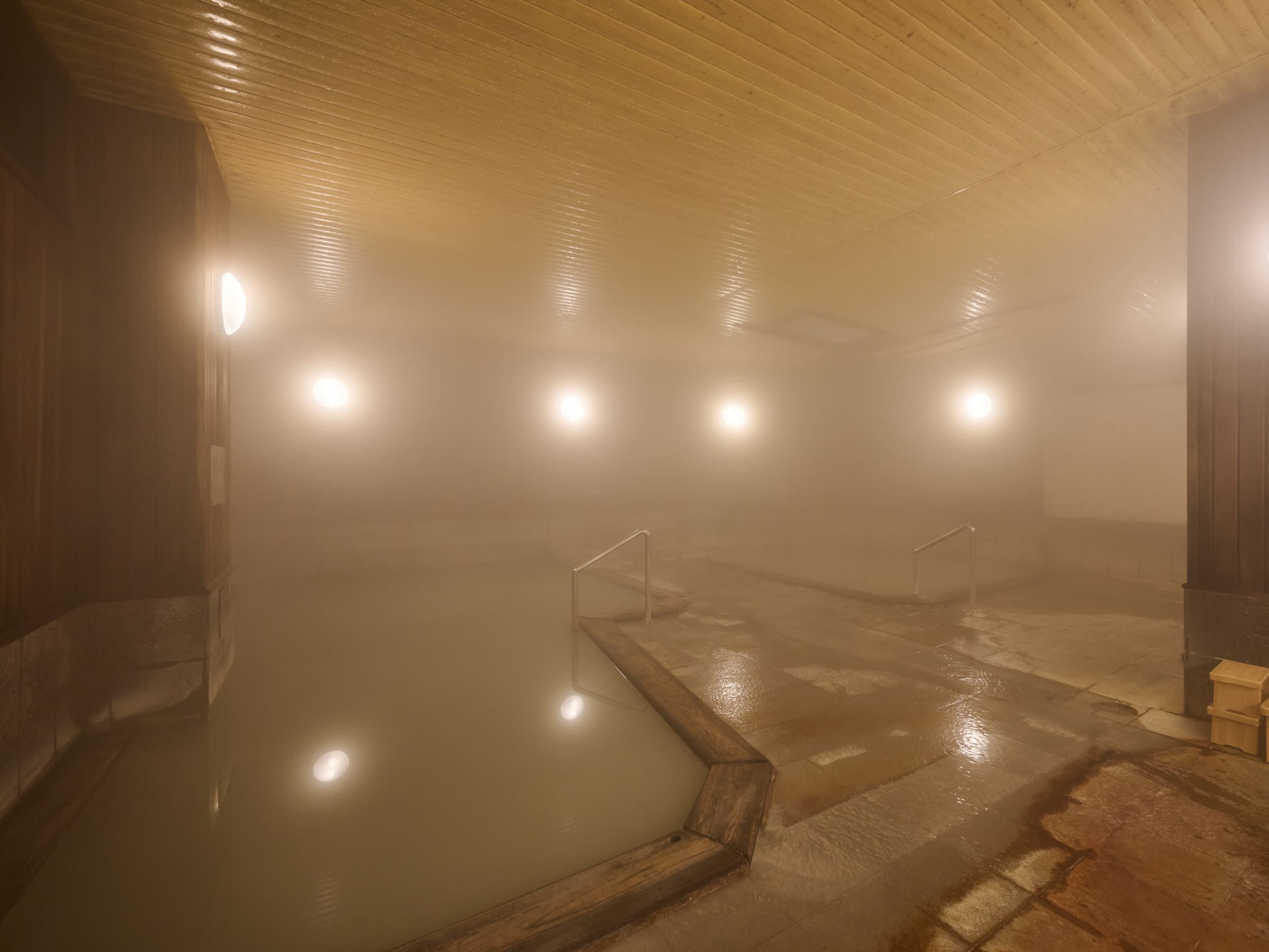 Steamy indoor onsen bath with milky hot spring water and wooden ceiling at Oyado Kiyomizuya, Noboribetsu