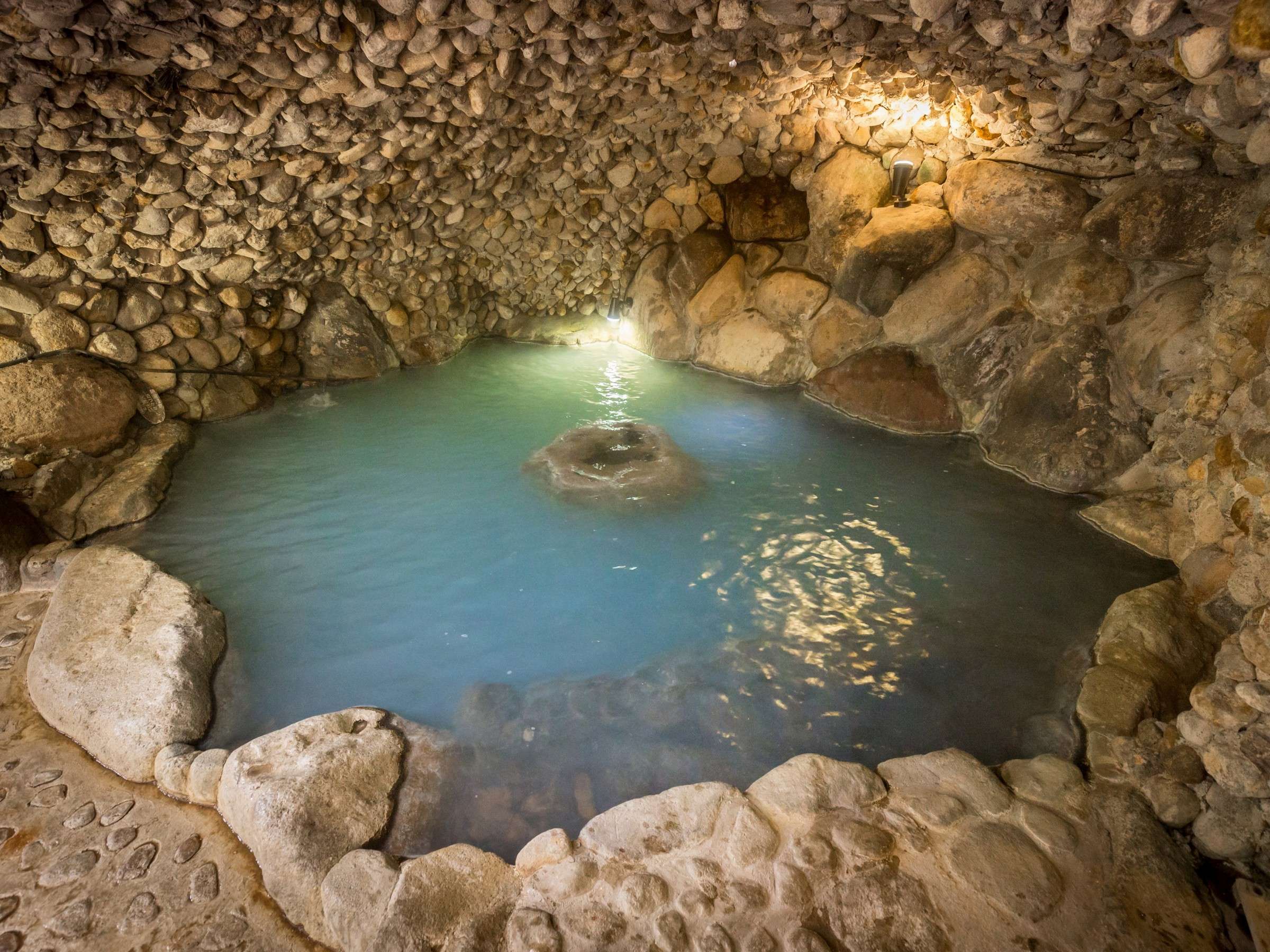 Anaburo cave bath at Satonoyu Waraku with turquoise hot spring water enclosed by rough natural stone walls