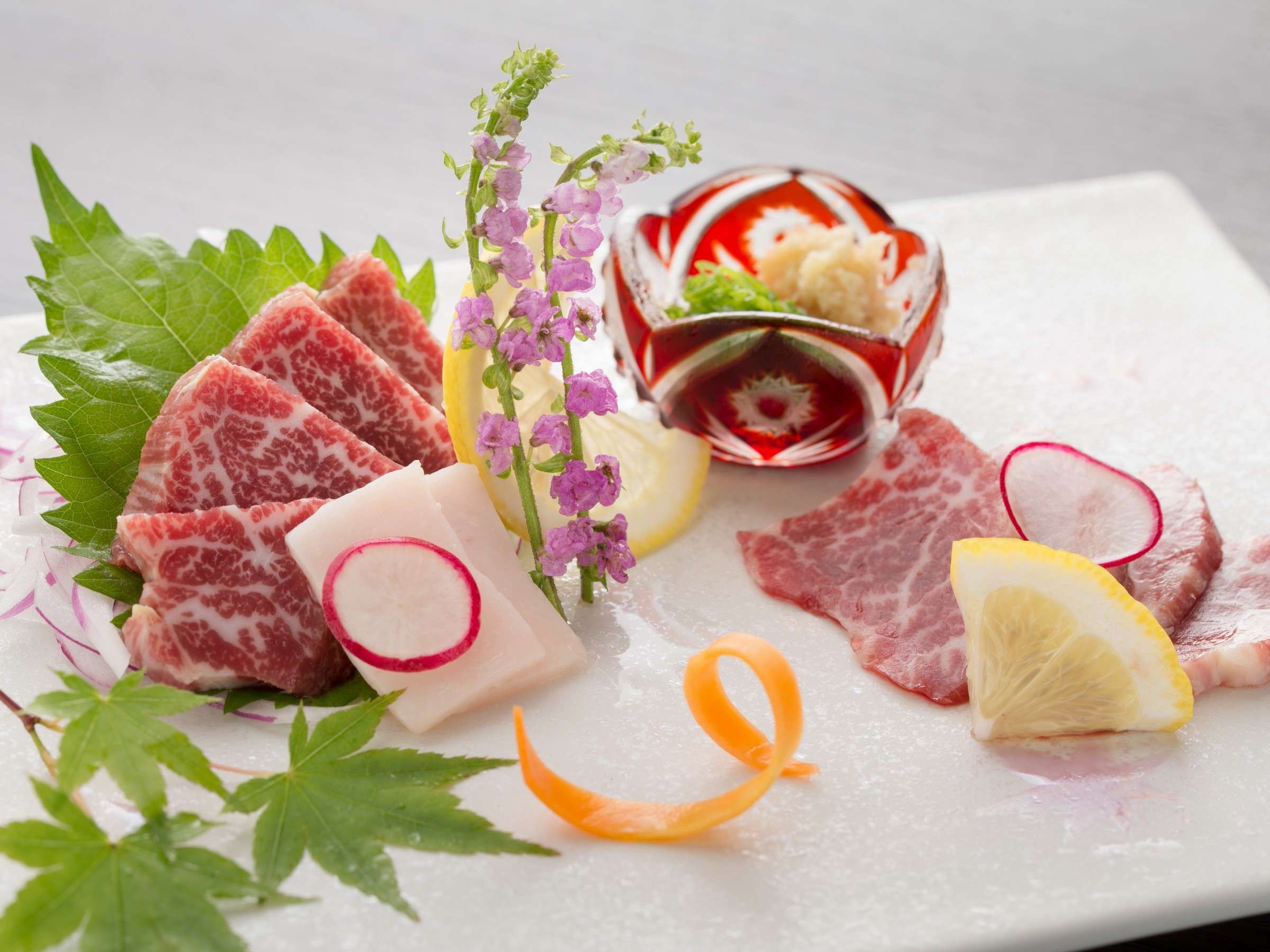 Plate of Kumamoto basashi horse sashimi at Satonoyu Waraku garnished with shiso, radish and edible flowers