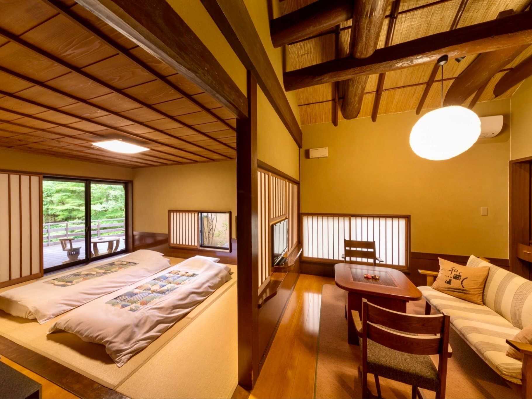 Japanese-style guest room at Satonoyu Waraku with futon laid out, exposed timber ceiling and a deck overlooking greenery