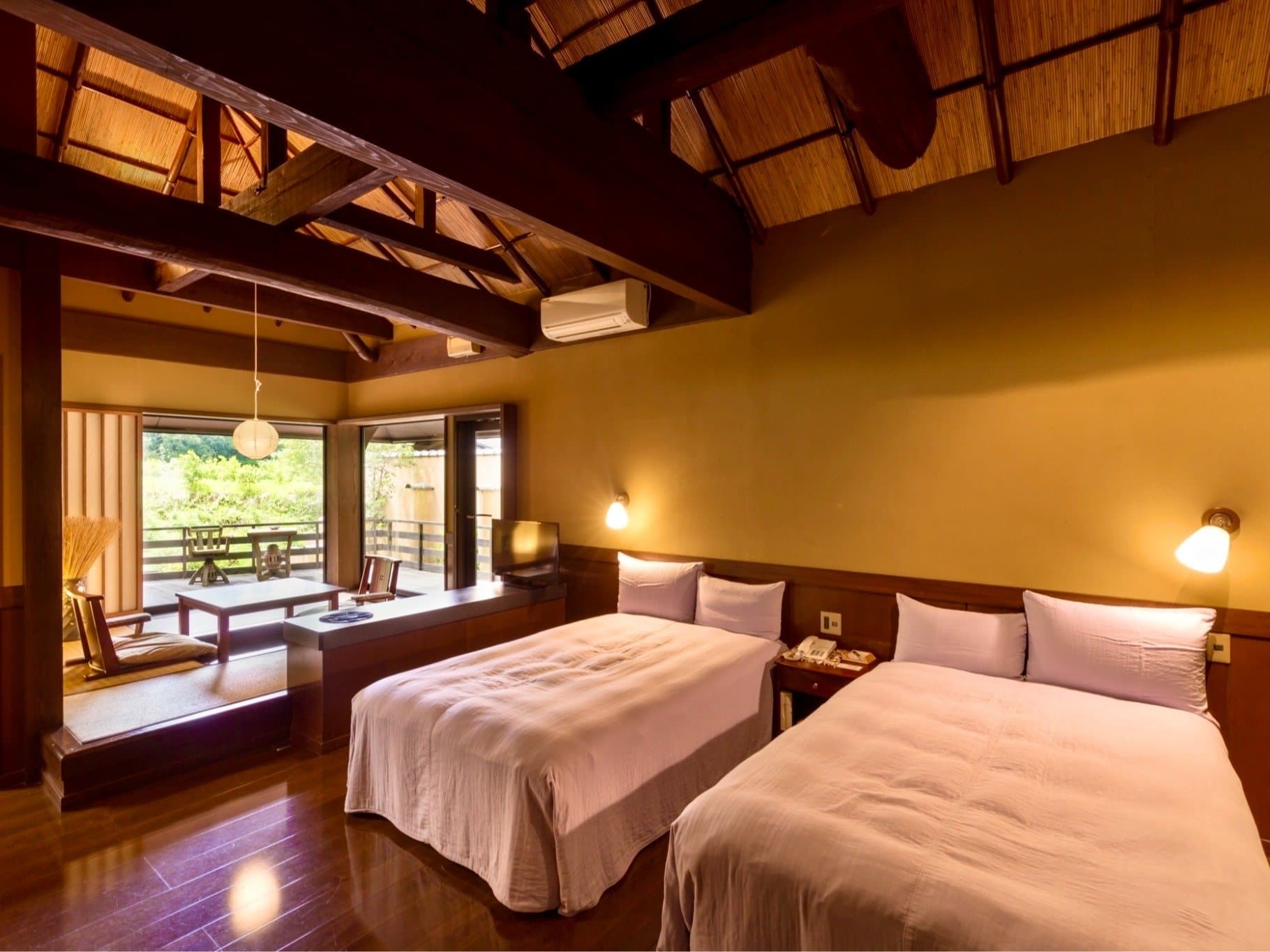 Western twin guest room at Satonoyu Waraku with two beds, raised tatami sitting nook and thatched timber ceiling