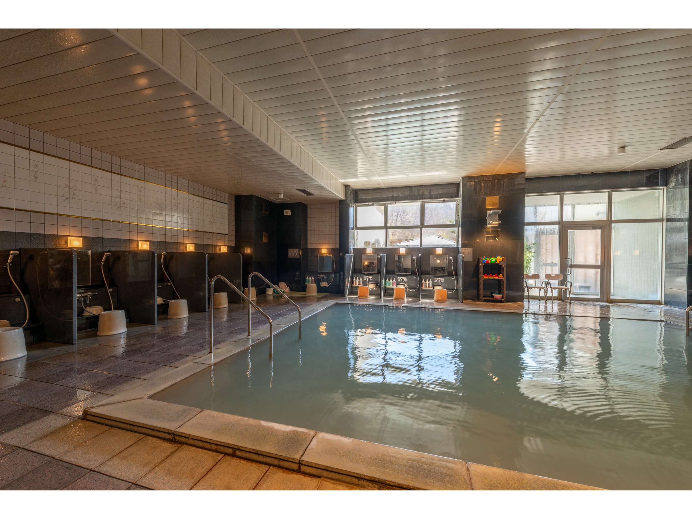 Spacious indoor onsen bath with large windows and tiled washing stations at Noboribetsu Manseikaku, Hokkaido