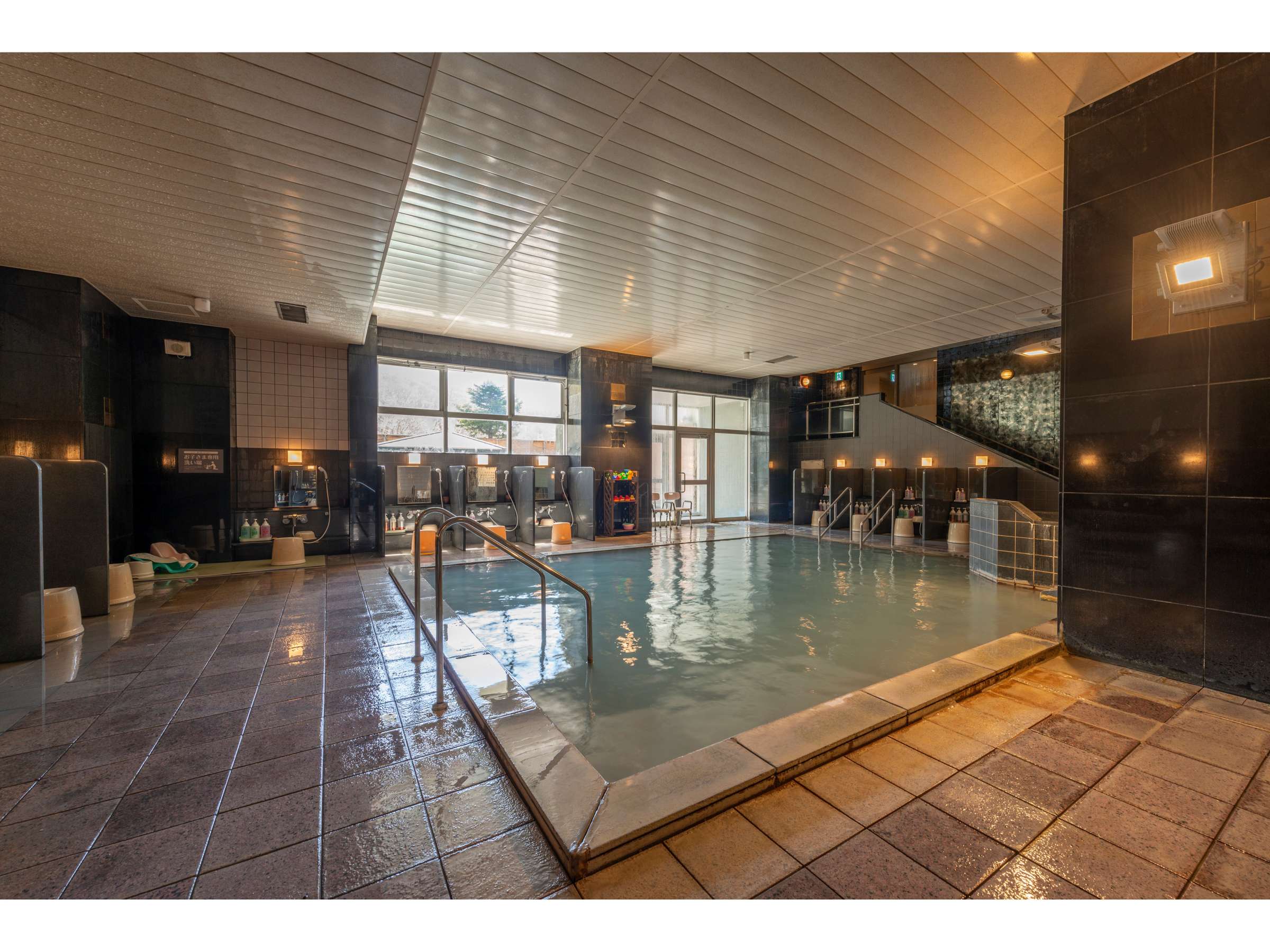 Indoor public bath with stone-tiled flooring and dark stone walls at Noboribetsu Manseikaku hot spring hotel