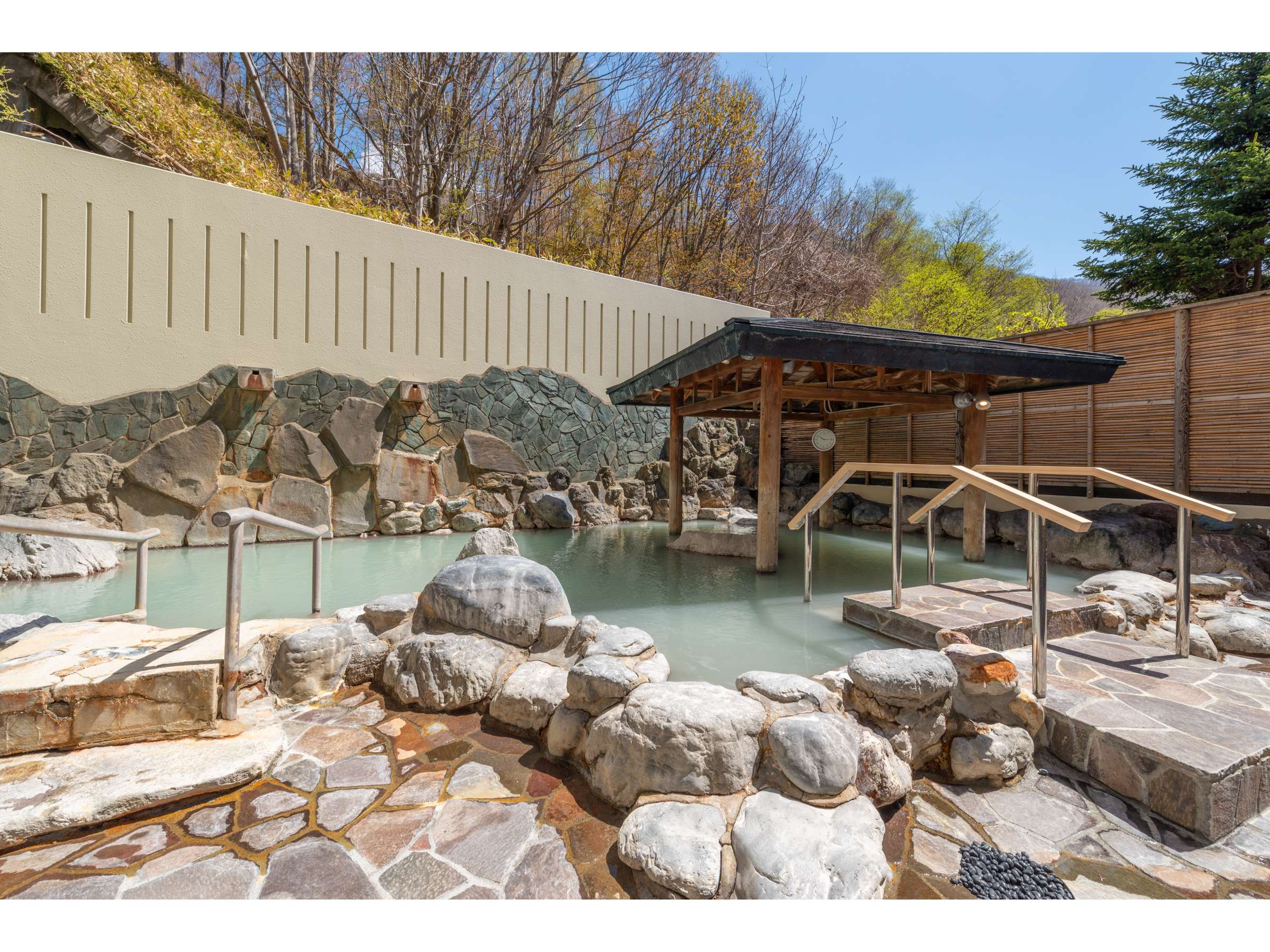 Outdoor rotenburo hot spring bath with milky onsen water, natural rock surround and a wooden roof at Noboribetsu Manseikaku