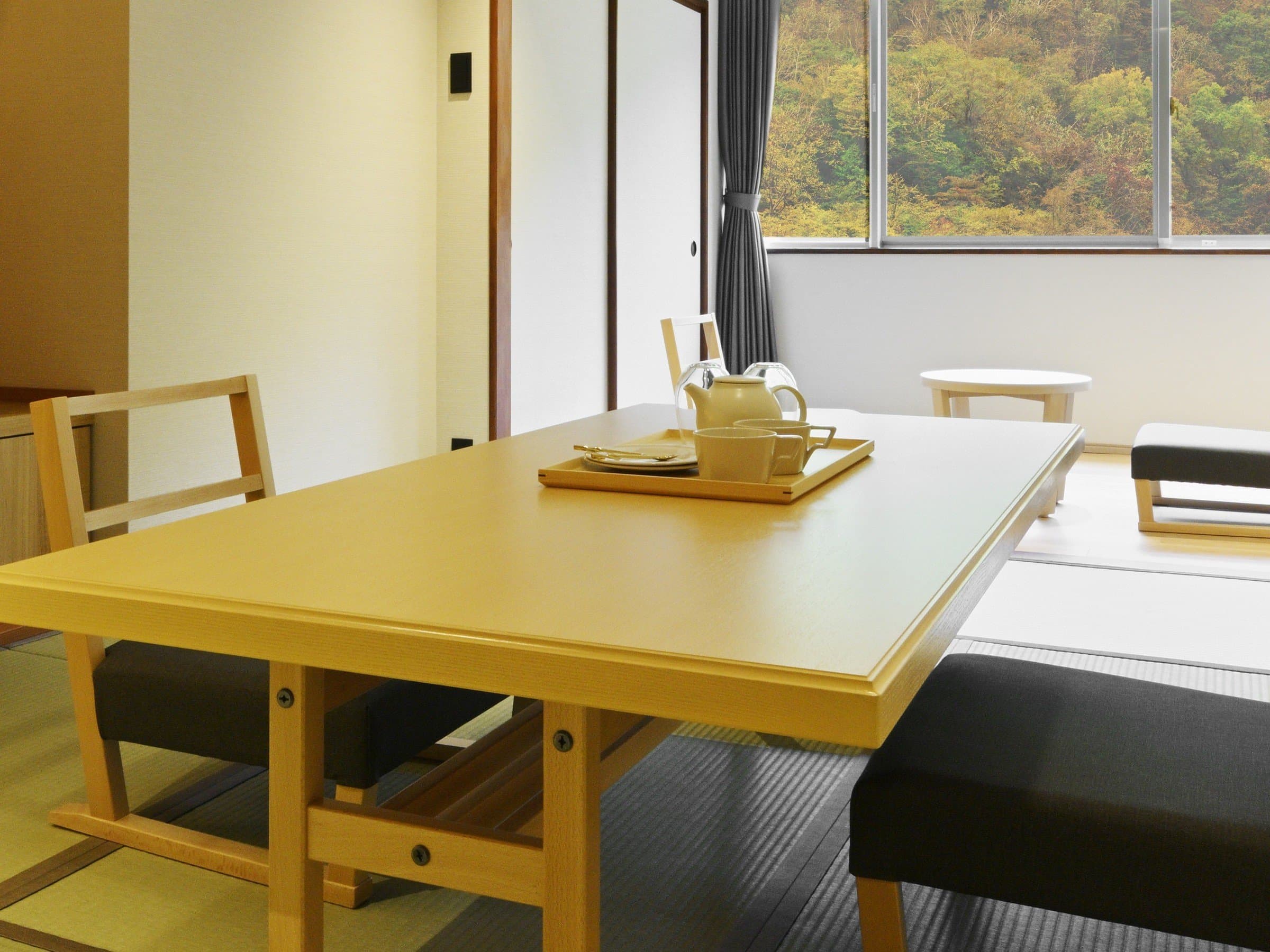 Japanese-style guest room with tatami floor, low wooden table and a window overlooking forested hills at Noboribetsu Manseikaku