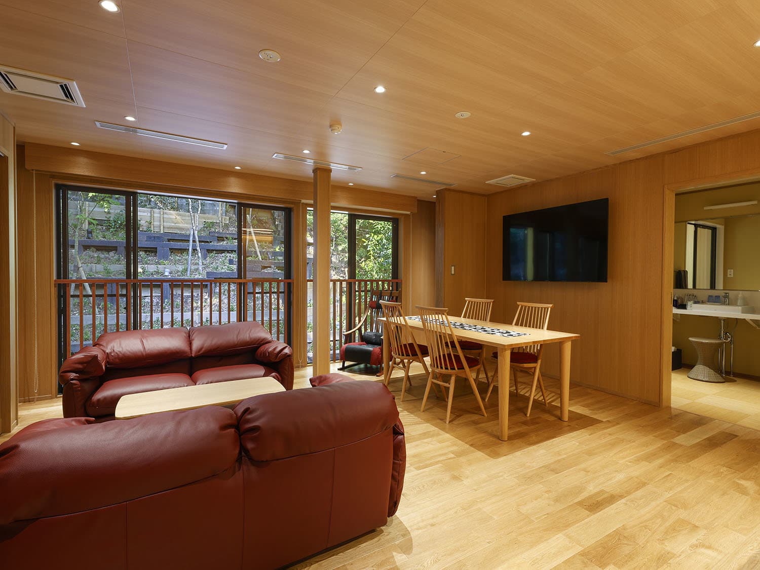Yuraku Kinosaki lounge with leather sofas, dining table and large windows overlooking greenery