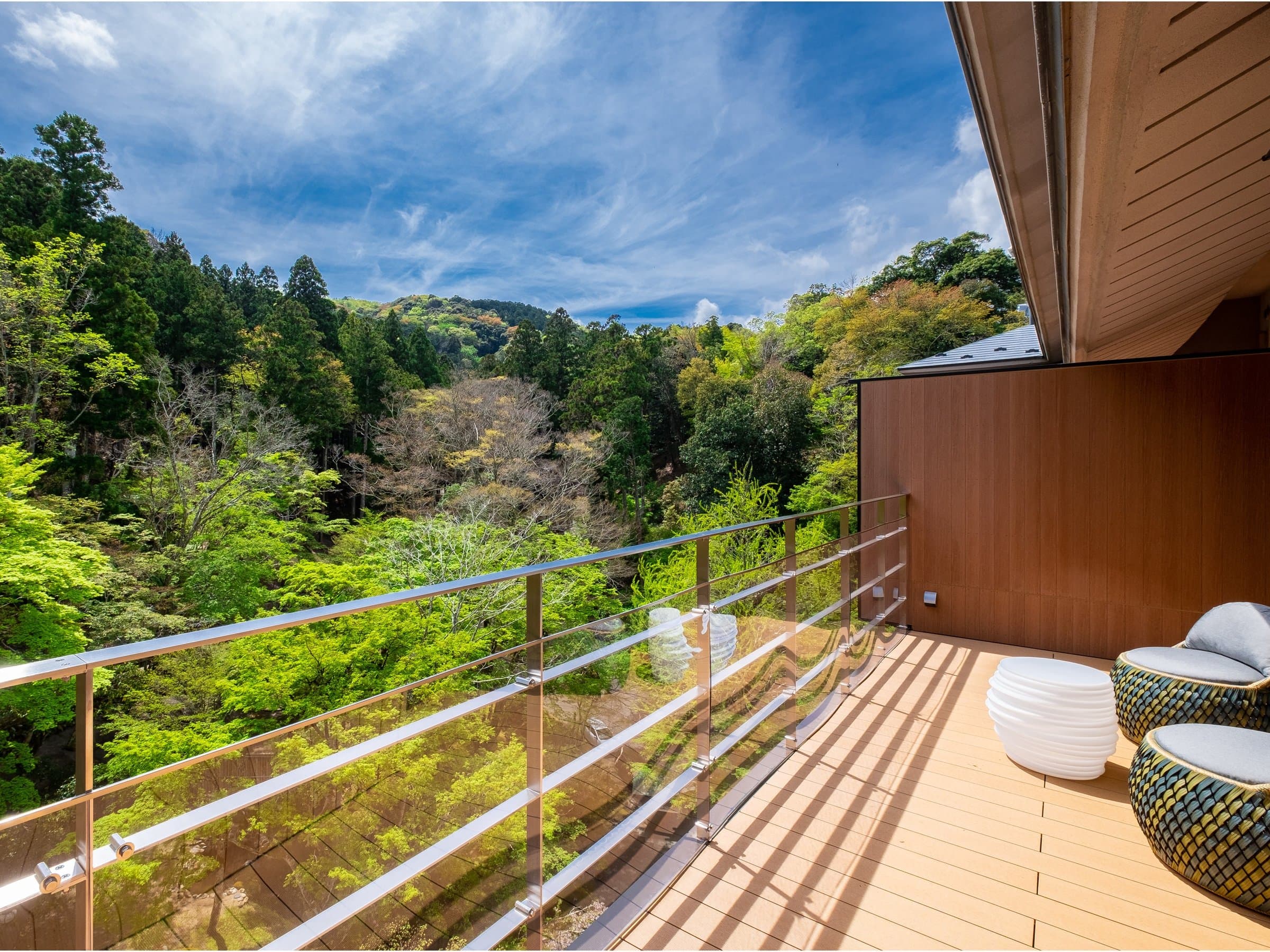 Sunny guest room balcony terrace with glass railing looking out over forested hills and blue sky at SORA Togetsuso Kinryu, Izu