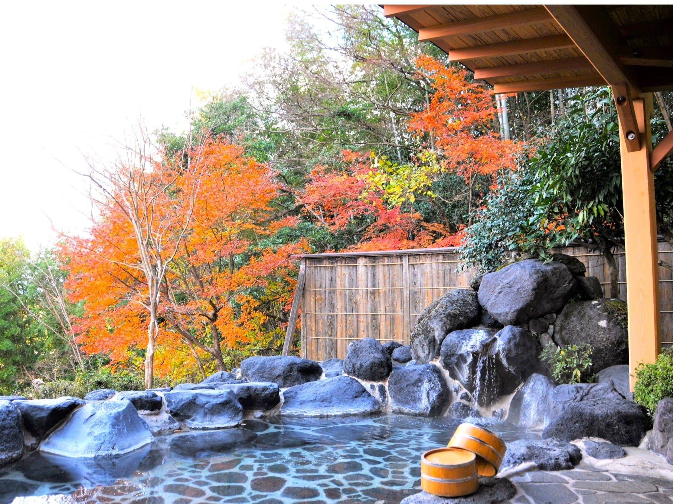 Outdoor rock onsen bath beneath brilliant red and orange autumn maple leaves at SORA Togetsuso Kinryu, Shuzenji Onsen, Izu