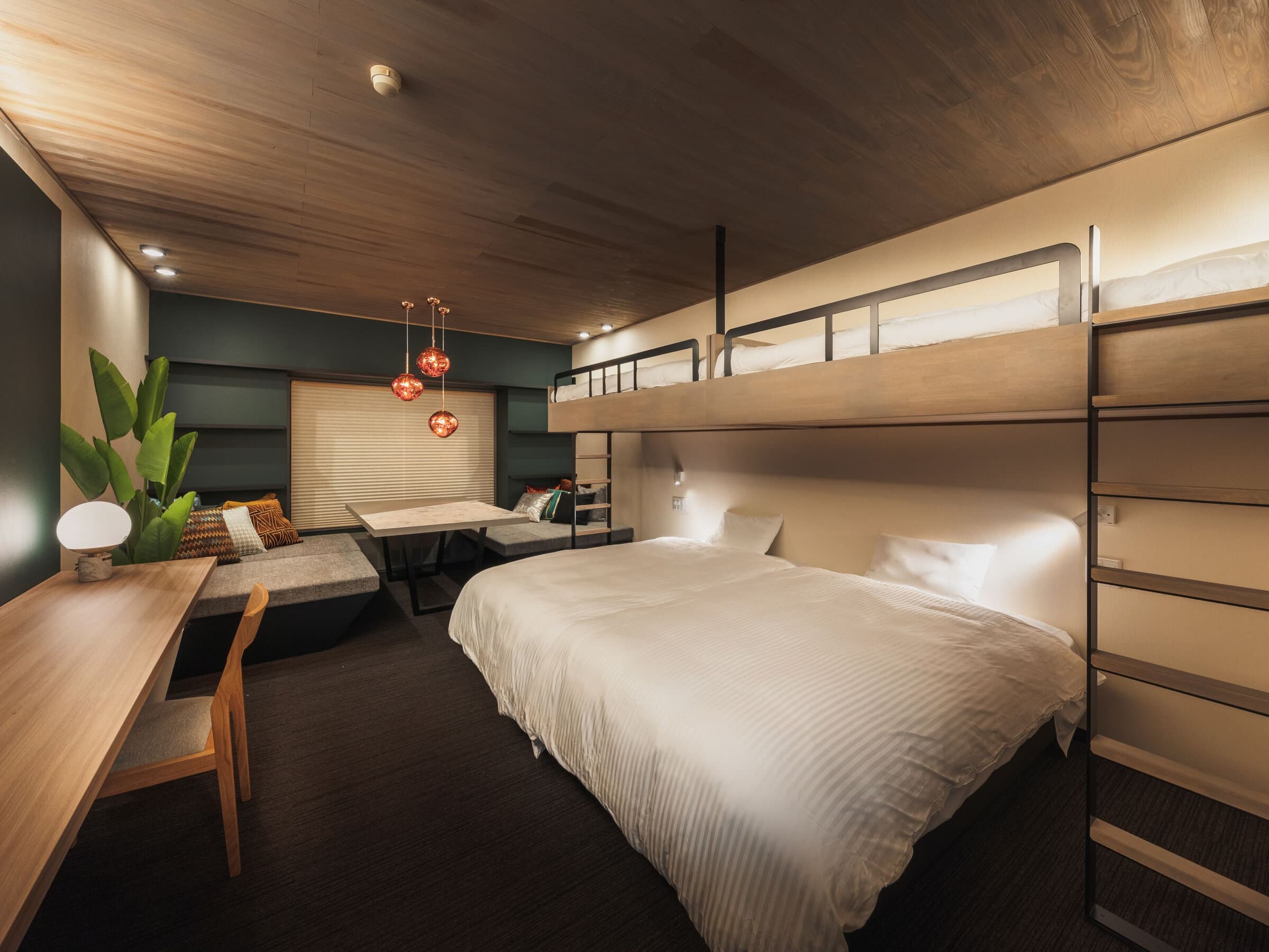Modern guest room at Hotel Jurin with a double bed, loft bunk and a sunken sofa nook under a wood ceiling