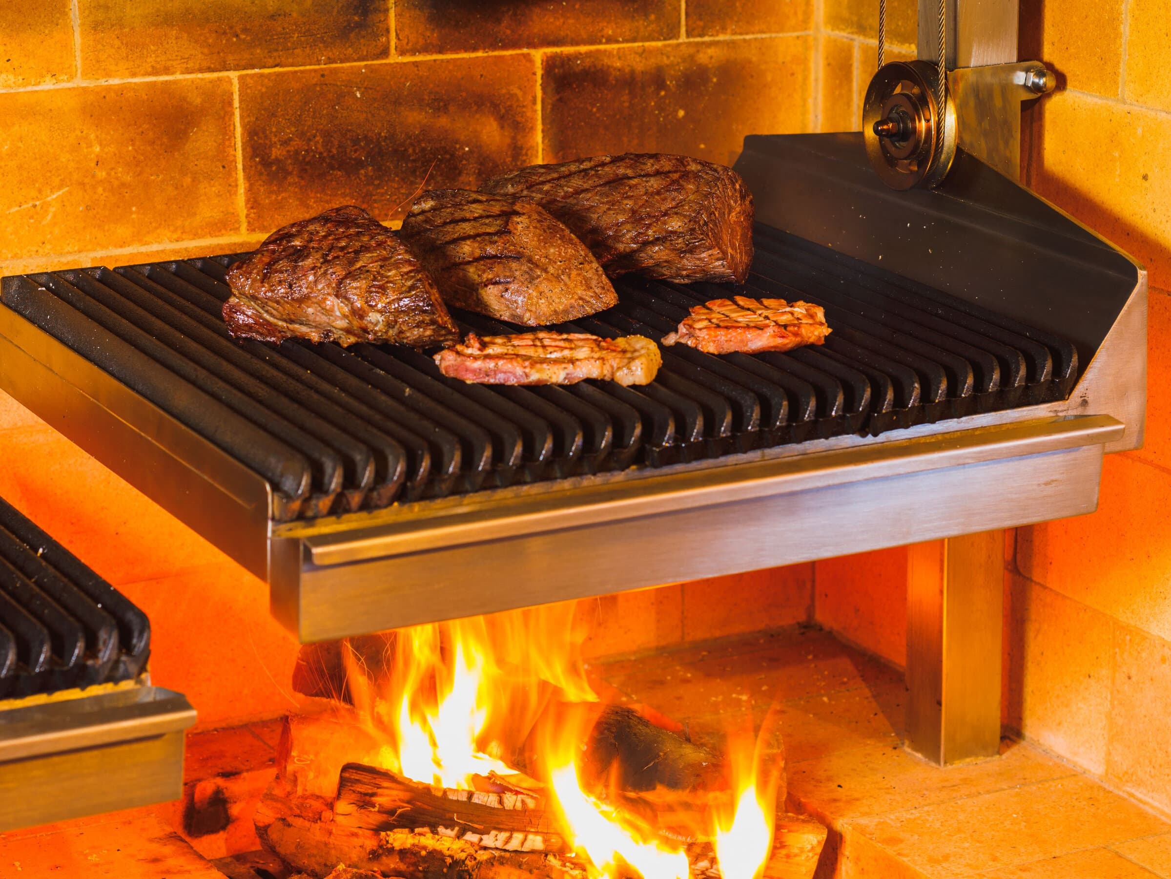 Steaks grilling over a wood-fired charcoal grill at Hotel Jurin's open kitchen