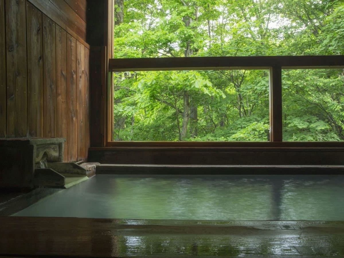 Hot-spring bath at Hotel Jurin framed by a window of fresh green forest in daylight