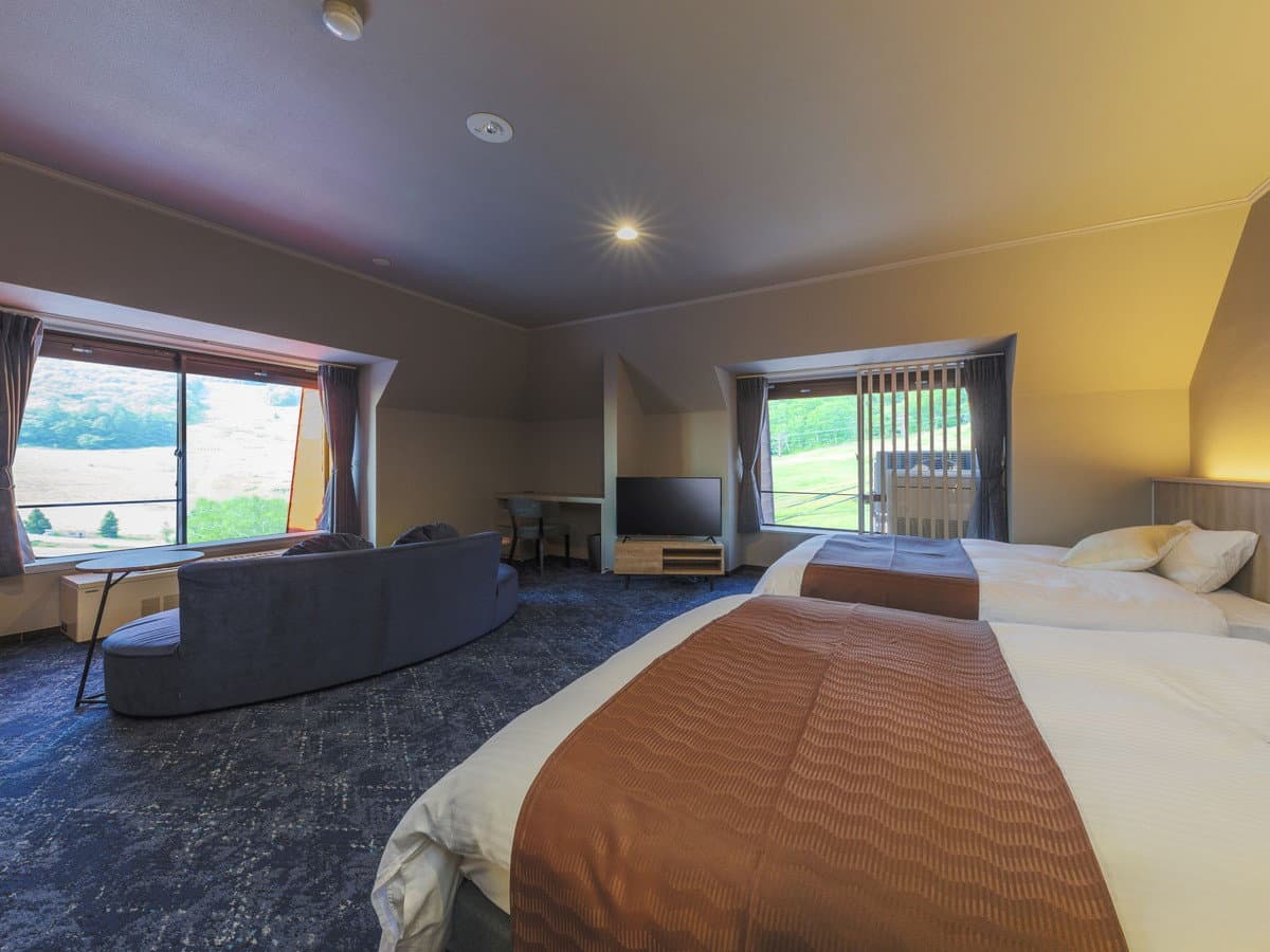 Spacious twin guest room at Hotel Jurin with a curved sofa and corner windows overlooking grassland and mountains