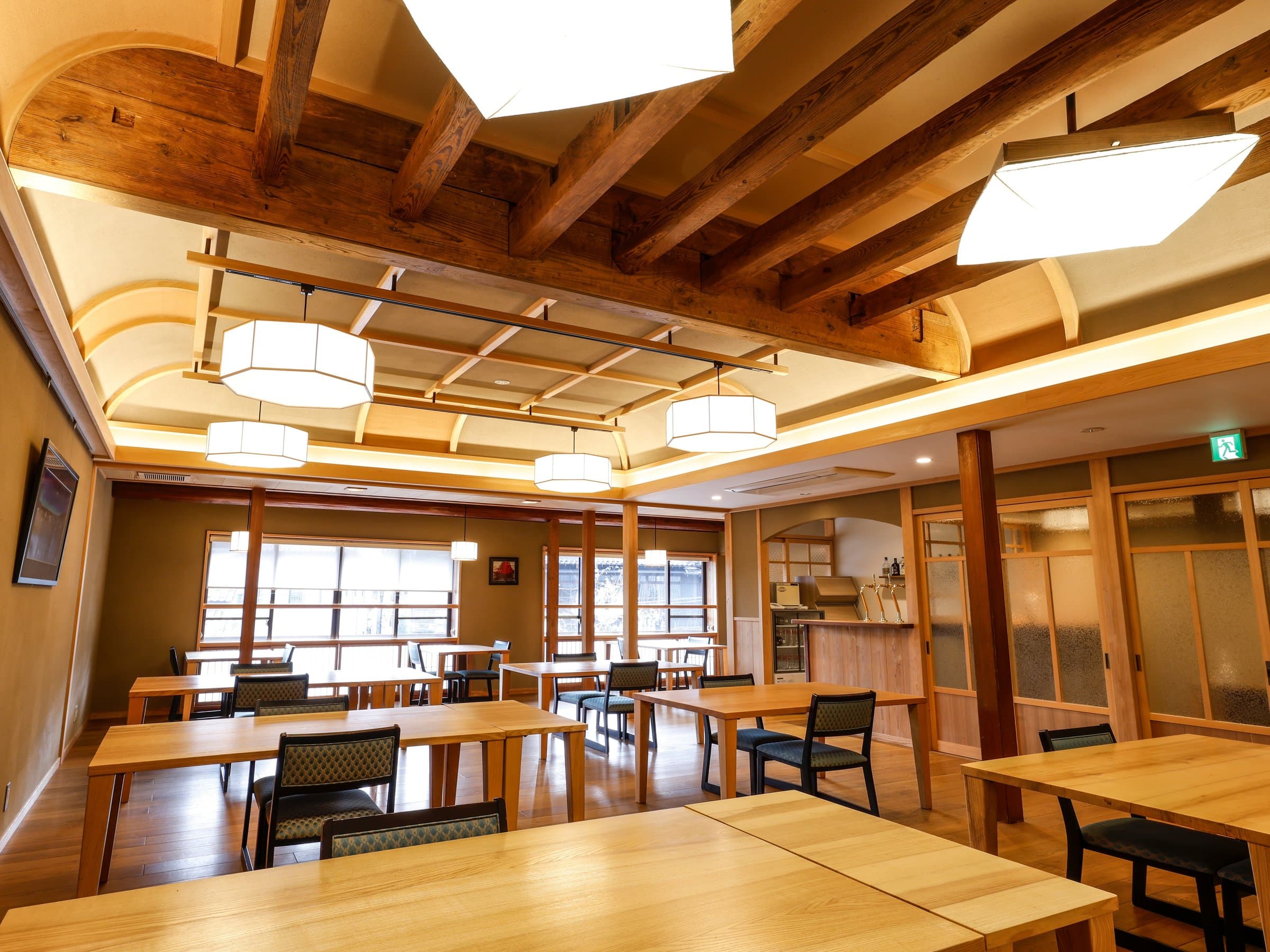Wide modern dining hall with light wood tables under exposed beams and paper lantern lights, Yamamotoya, Kinosaki Onsen