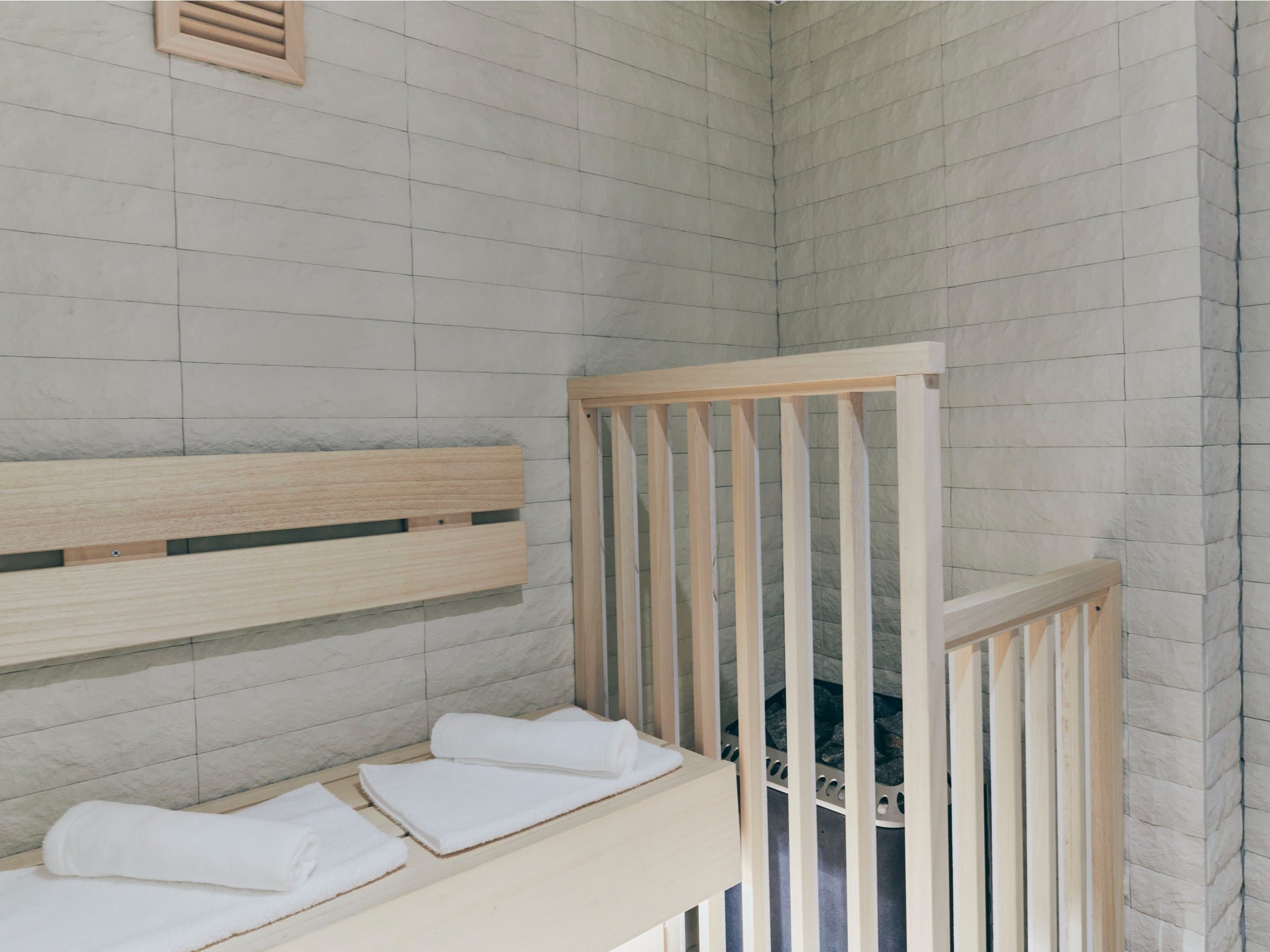 Wood-lined private sauna with stone heater and rolled white towels at Korinkyo Kanazawa