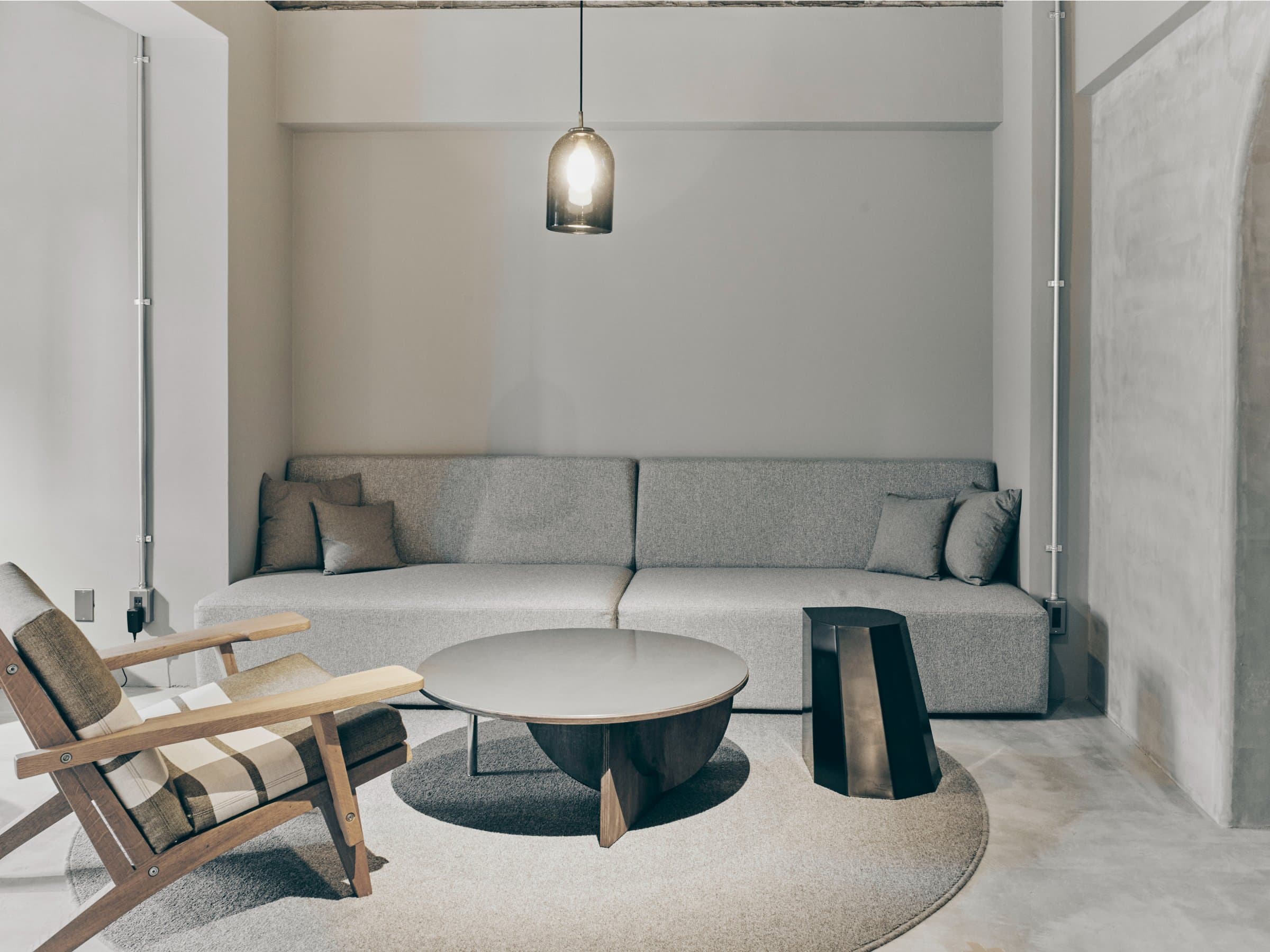 Minimalist lounge at Korinkyo Kanazawa with a grey sofa, wooden lounge chair, round table and pendant lamp