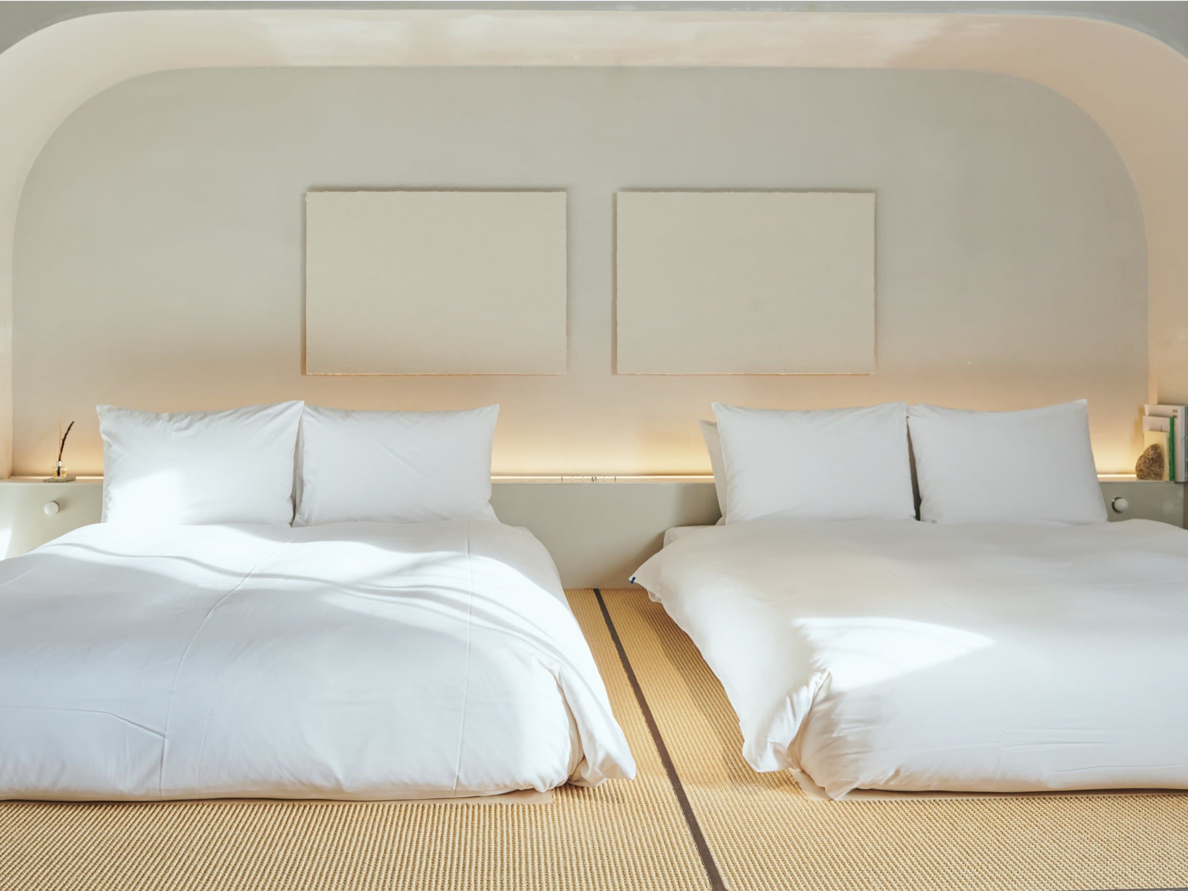 Twin beds with white linen and a soft curved headboard on a tatami-style mat floor at Korinkyo Kanazawa