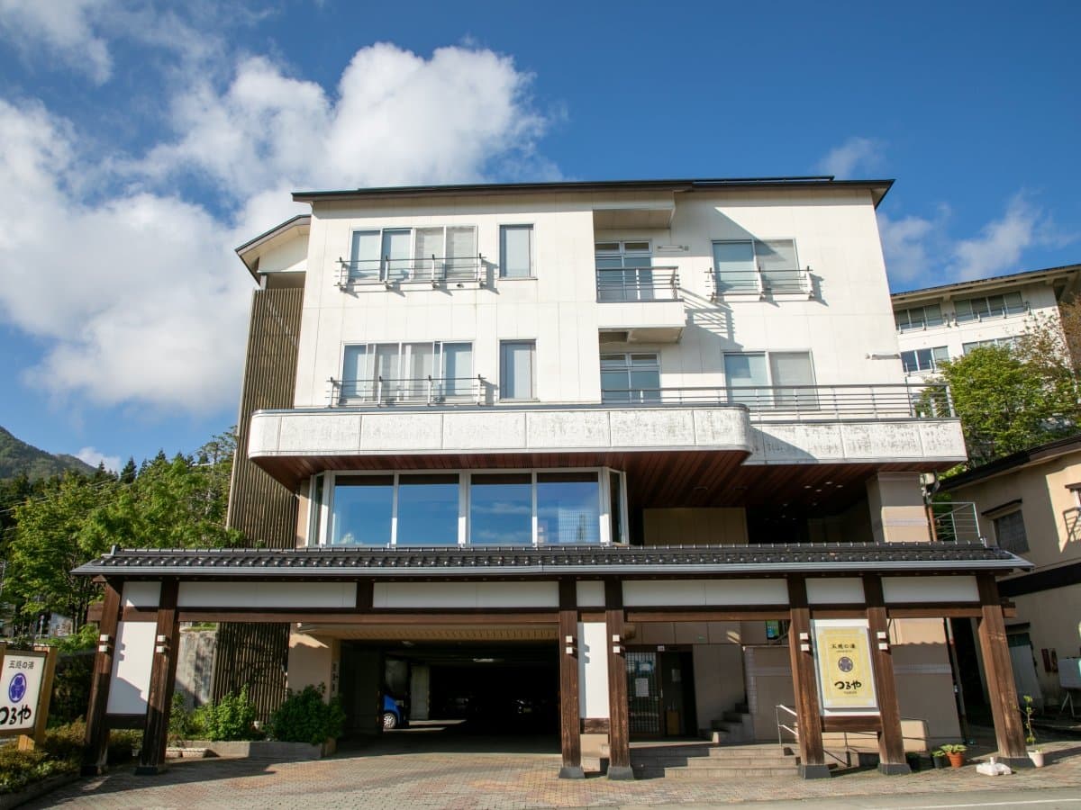 Full exterior of the four-story Gokan no Yu Tsuruya building under a blue summer sky in Zao Onsen