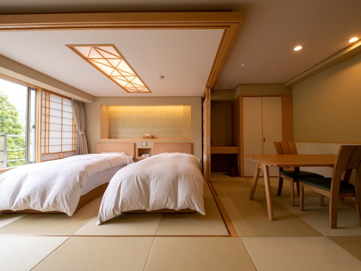 Spacious tatami guest room with twin beds and a wooden dining set at Gokan no Yu Tsuruya