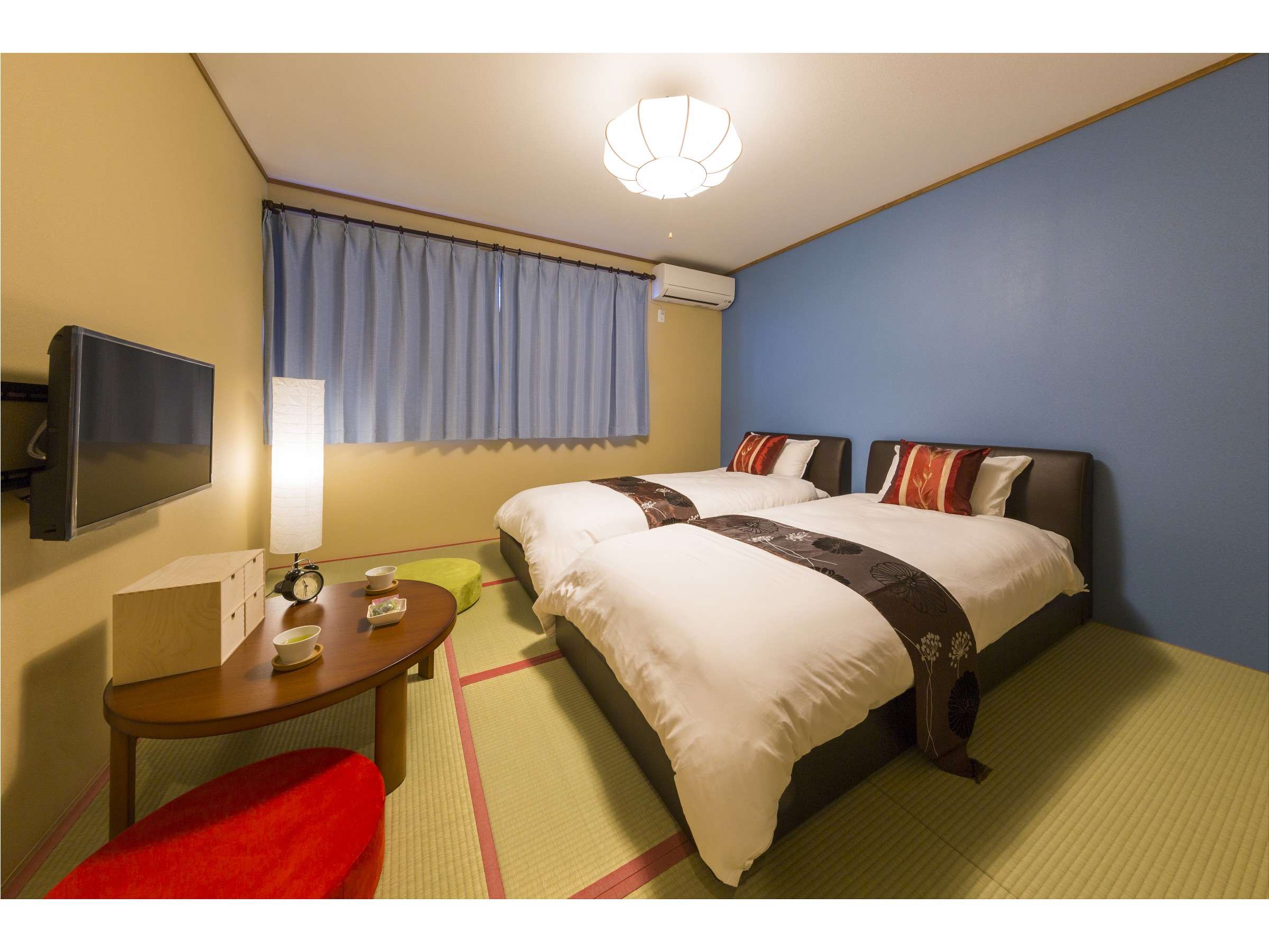 Twin-bed tatami room with blue feature wall, blue curtains and a round wooden tea table