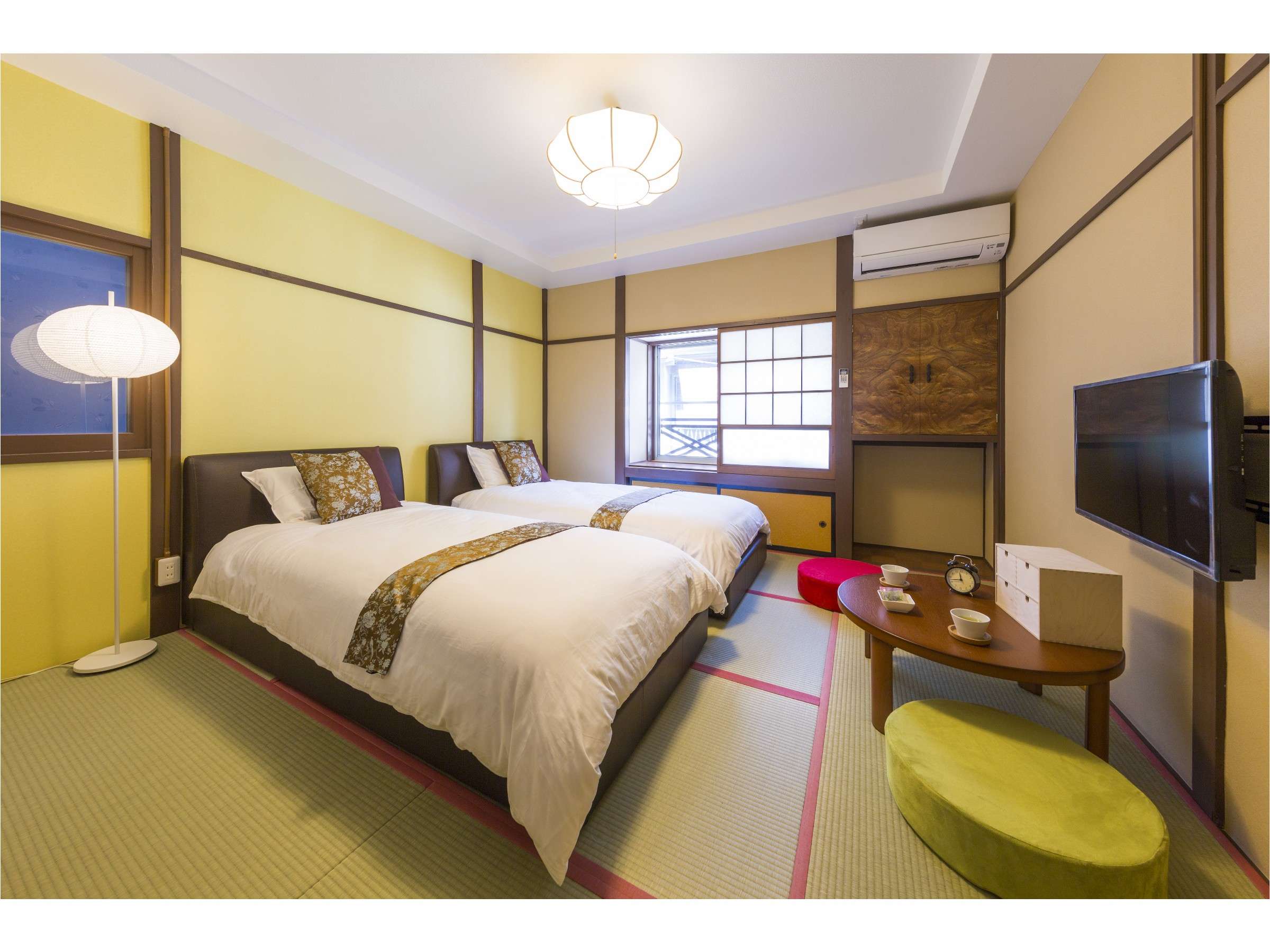 Tatami guest room with two beds, yellow walls, hanging lantern light and wall-mounted TV