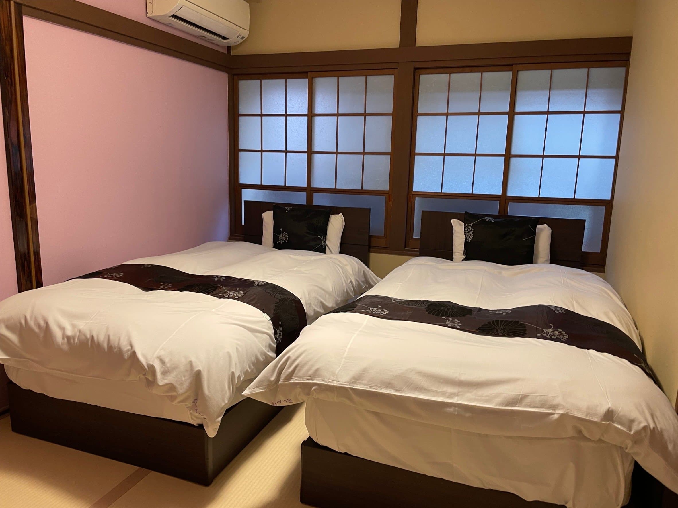 Twin-bed Japanese room with soft pink wall and tall latticed shoji windows