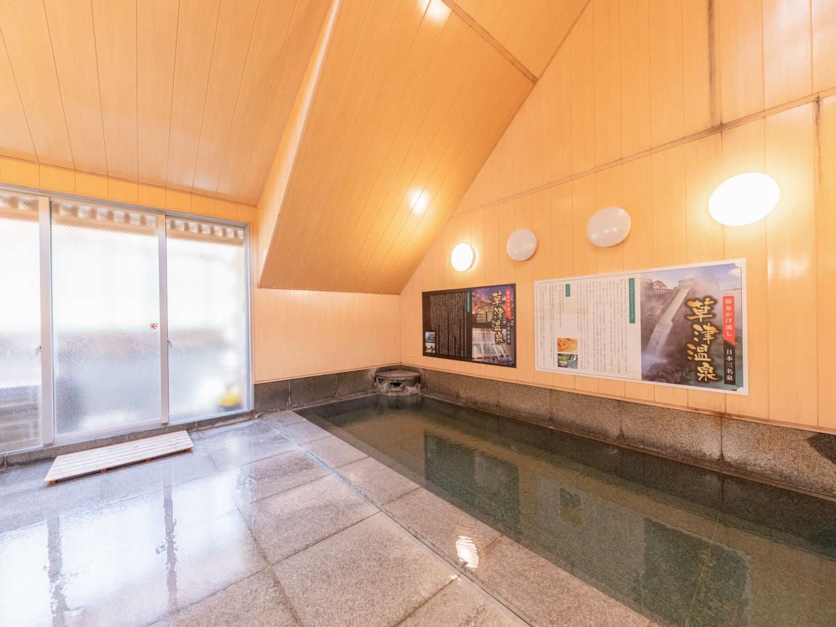 Indoor public onsen bath under a sloped wood ceiling with a stone-rimmed pool