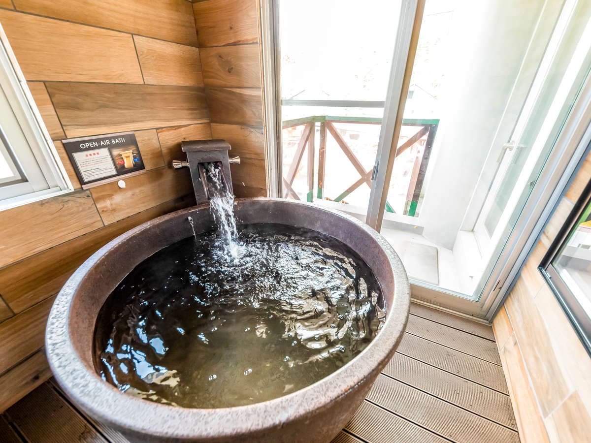 In-room semi-open-air Shigaraki-ware round bath on a wooden balcony with thermal water pouring in
