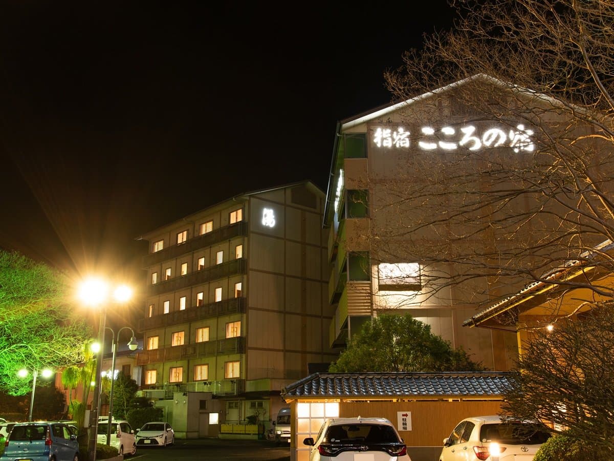 Ibusuki Kokoro no Yado illuminated at night, the inn facade lit with its name signage and a warm-glowing onsen wing