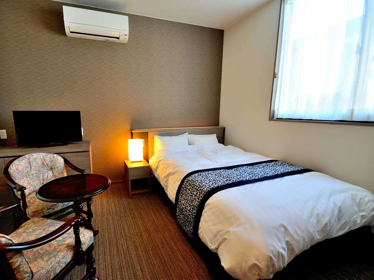 Oyado Yukizumi single guest room with white-linen bed, bedside lamp, TV and floral armchairs