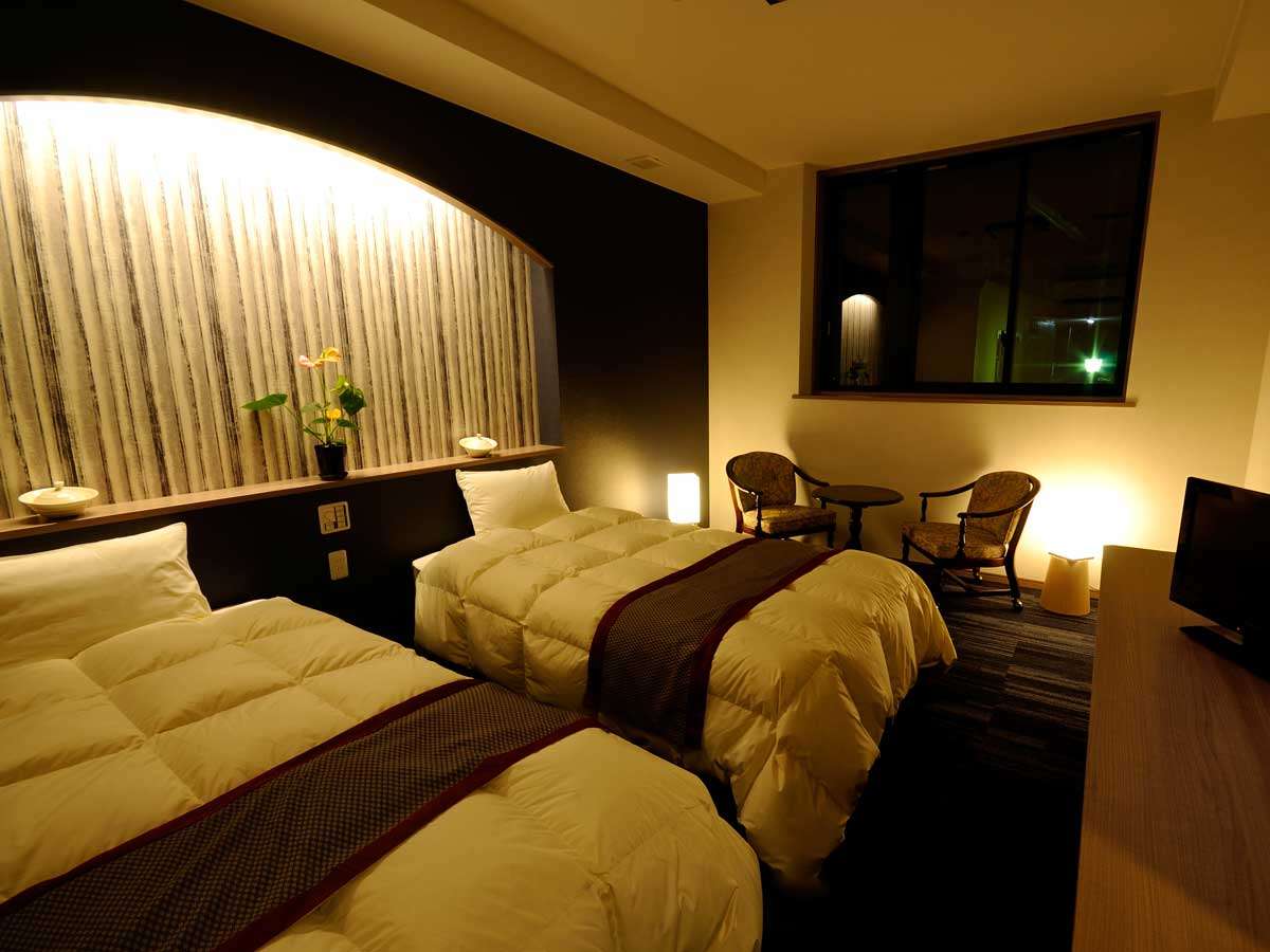 Oyado Yukizumi twin guest room at night with warm lighting, arched headboard alcove and lounge chairs