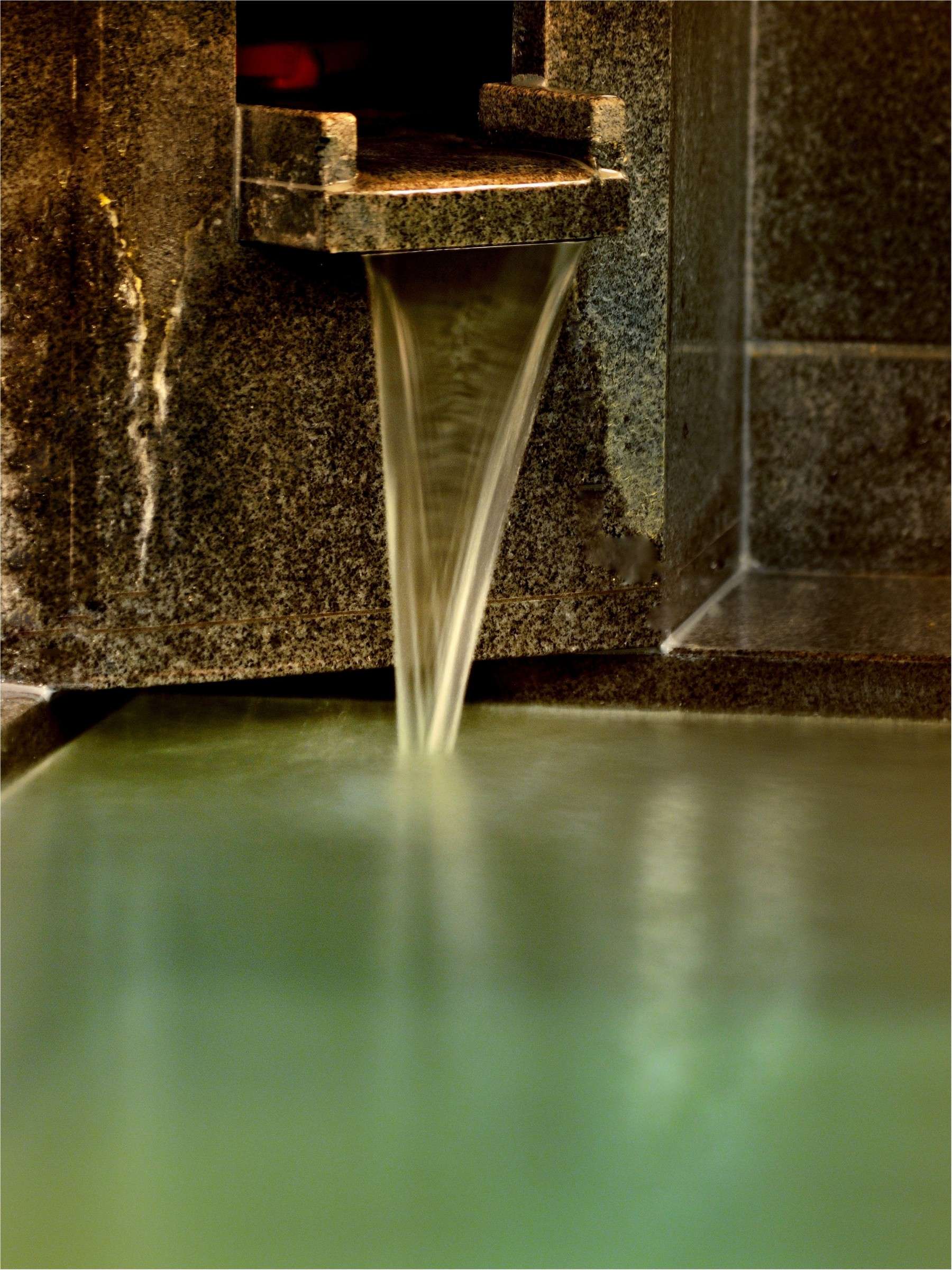 Oyado Yukizumi onsen detail, Yubatake-source water pouring kakenagashi from a stone spout into a green-tinted bath