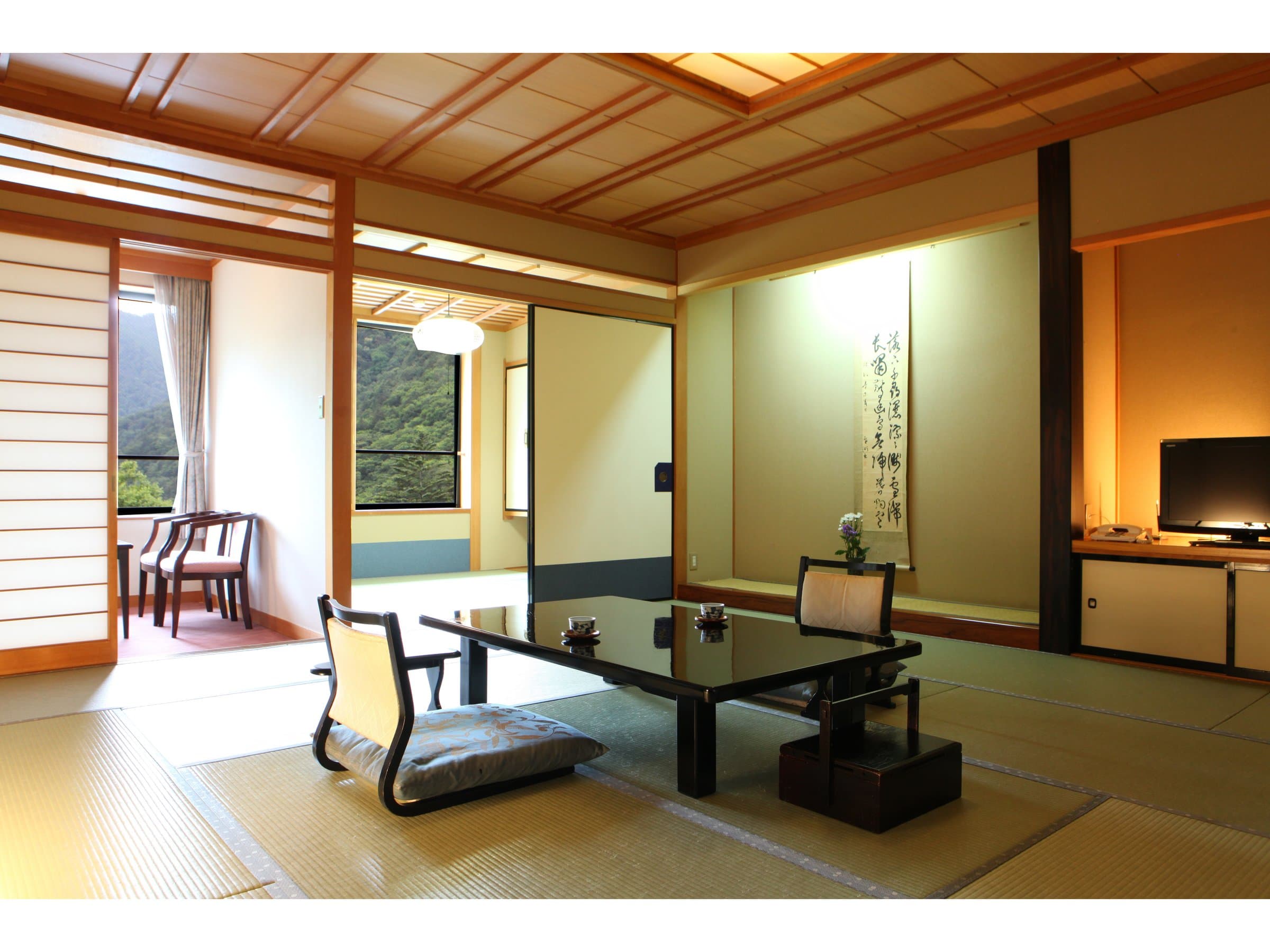 Spacious tatami guest room with a calligraphy scroll, low table and TV alcove at Shirafuneso Shintaku Ryokan in Shirahone Onsen