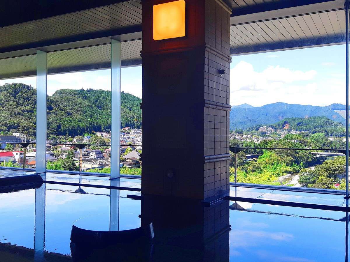 Indoor onsen bath beside large windows overlooking the forested hills and river town of Ome