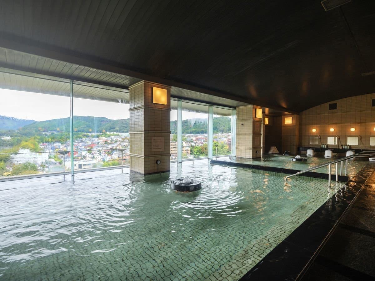 Wide hot-spring bathing hall with washing stations and panoramic mountain-view windows at Kamenoi Hotel Ome